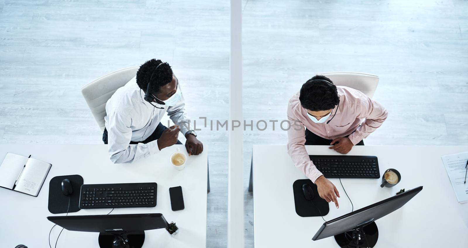 Assisting each other from a safe distance. High angle shot of two call centre agents working together in an office. by YuriArcurs