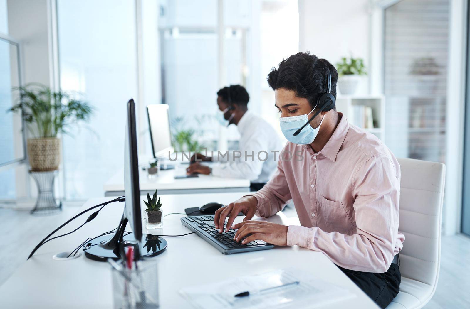 Its back to business. a young call centre agent wearing a face mask while working on a computer in an office