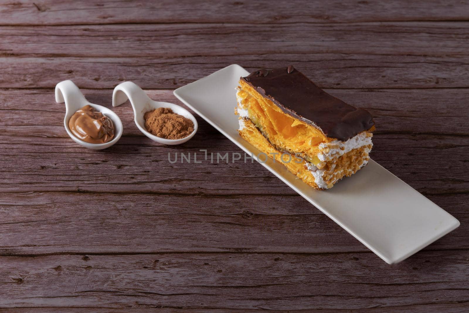 puff pastry cake with cream and almonds covered with chocolate with spoons with its ingredients and copy space