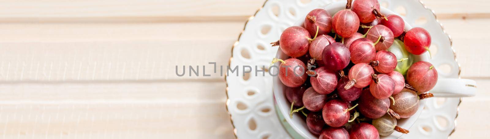 Fresh, sweet red gooseberries in a white cup on a white background.