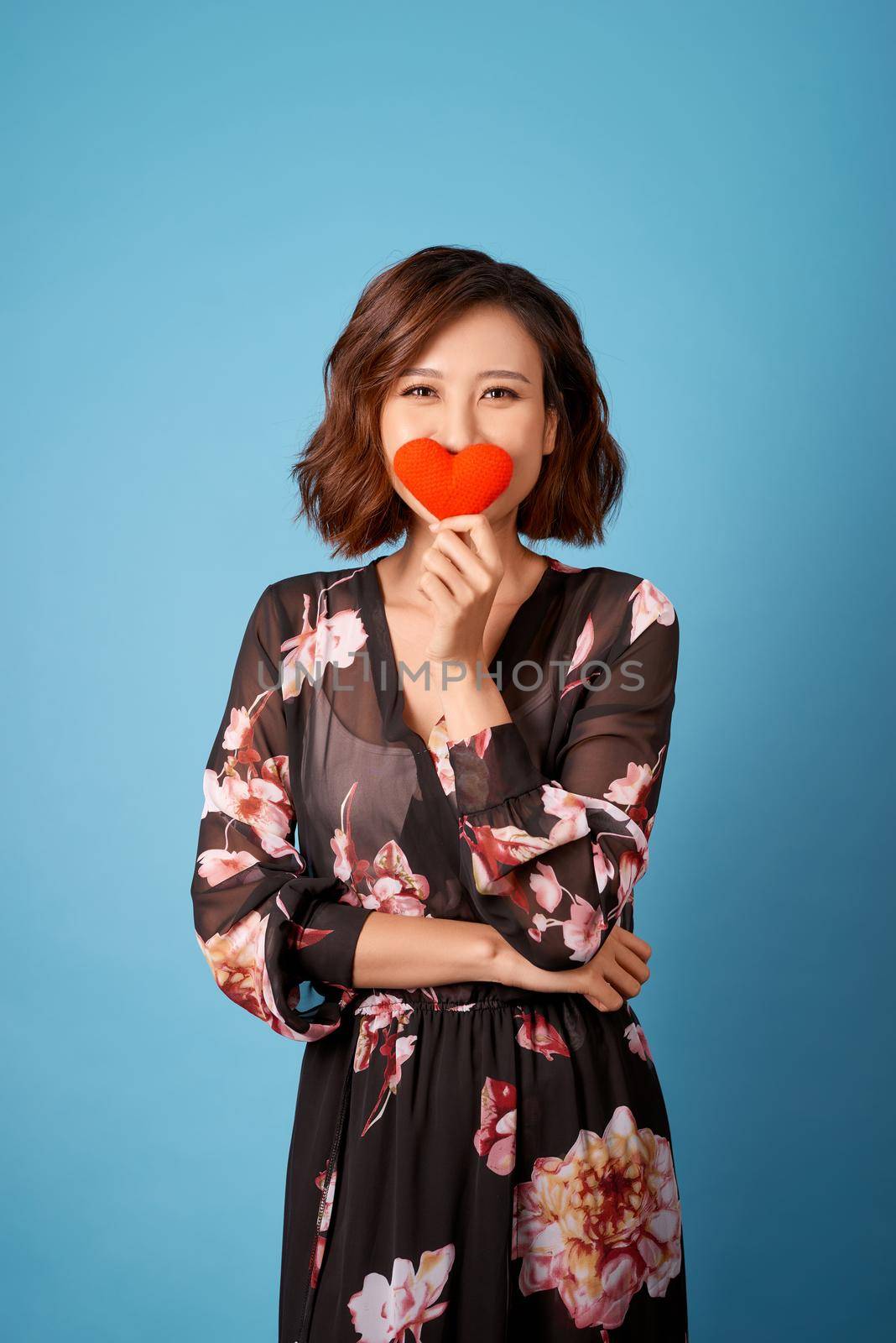 Asian woman holding red heart cover her face isolated on light blue background. 