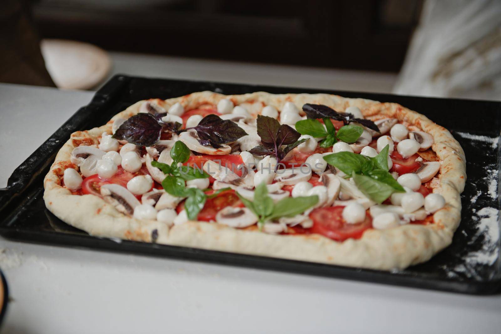 Appetizing raw Italian vegetarian pizza with fresh organic ingredients: sliced champignons, ripe juicy tomatoes, mozzarella cheese and feta in the sides on a pizza pan, on a white table background