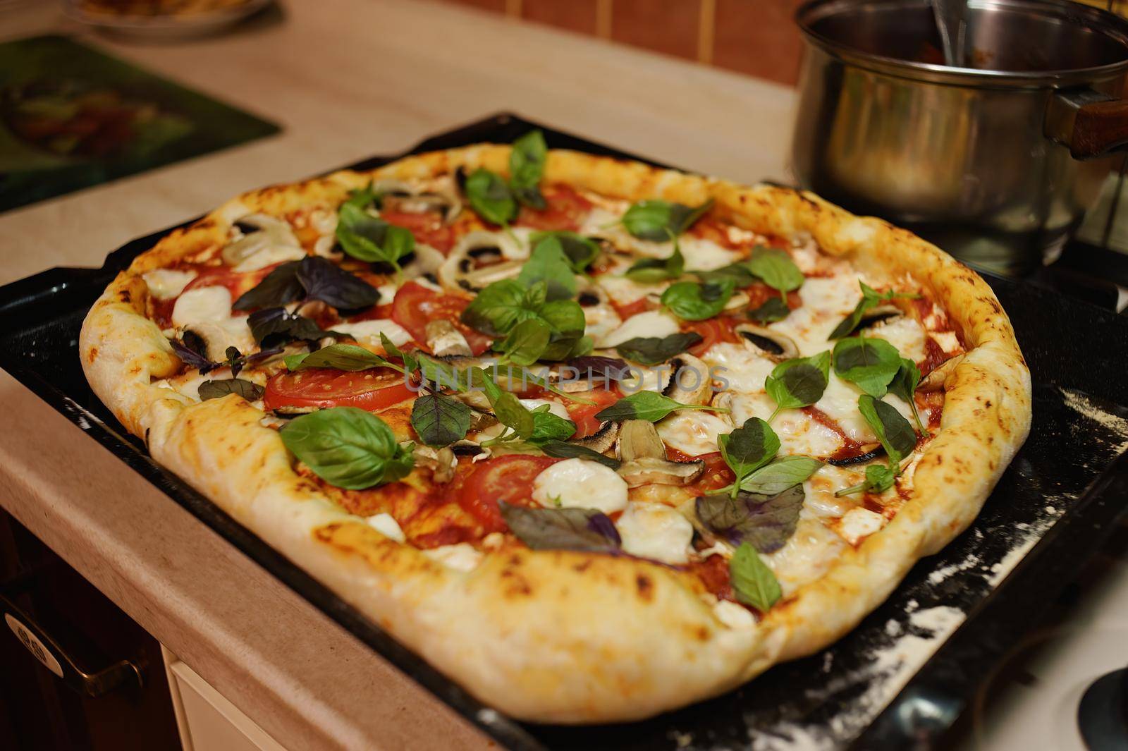 Top view. Freshly baked Italian pizza with mozzarella cheese and fresh leaves of basil, on baking sheet just taken out of oven on a kitchen worktop