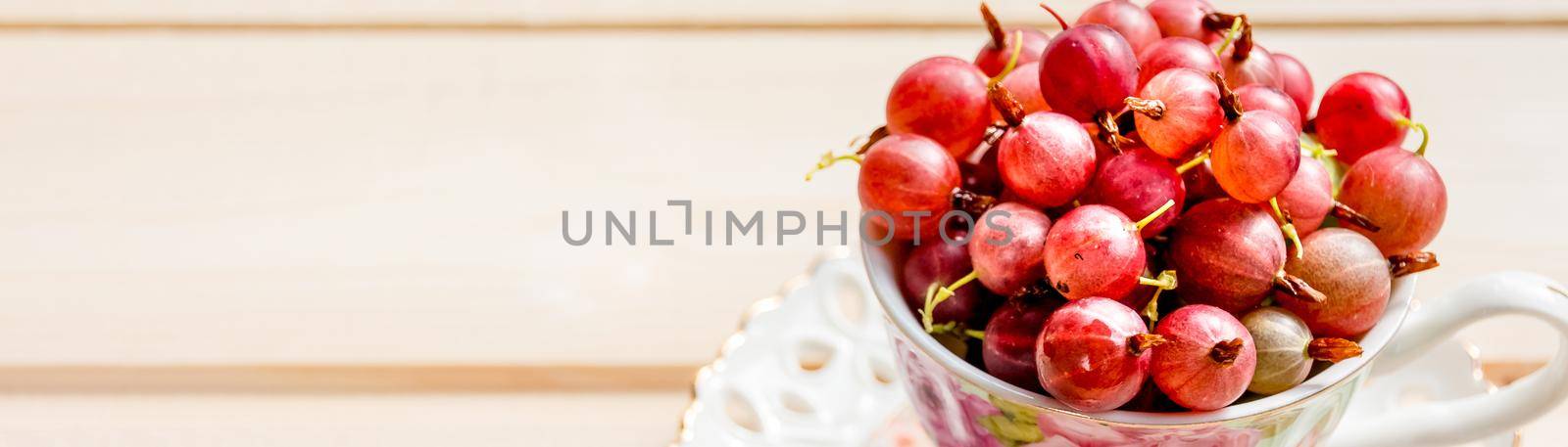 Fresh, sweet red gooseberries in a white cup on a white background.