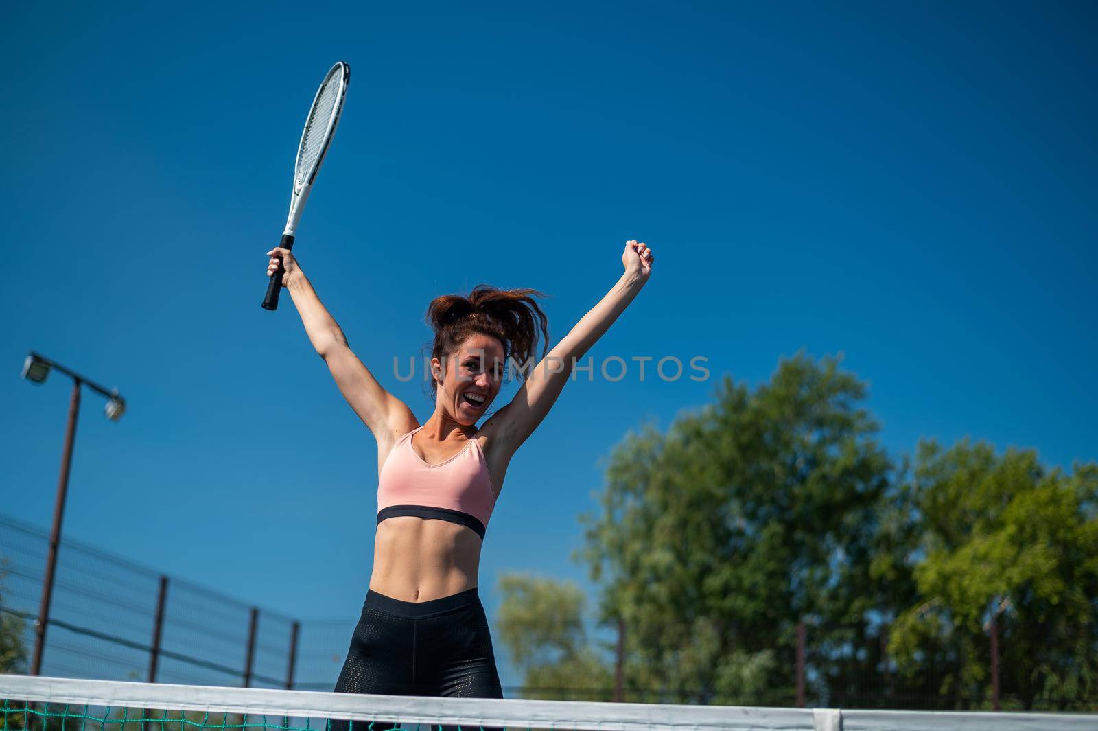 The female winner celebrates her tennis success. The happy girl is jumping on outdoors tennis court