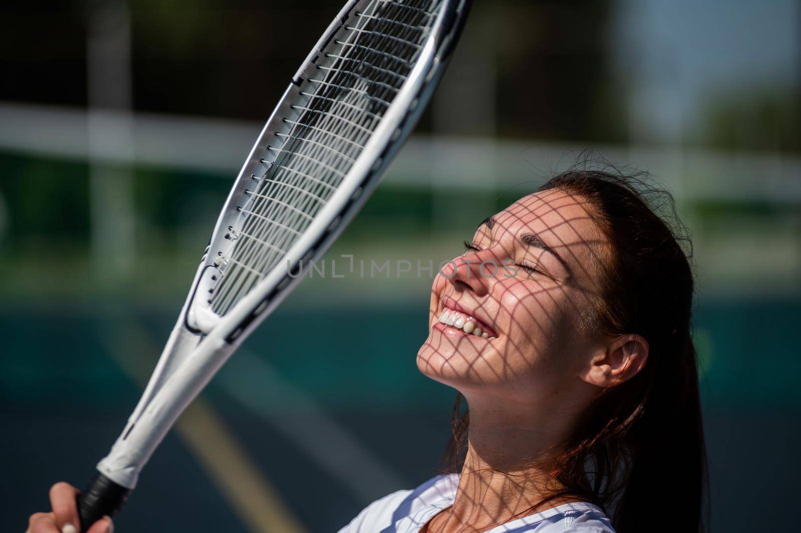 Beautiful smiling woman with a shadow from a tennis racket on her face on a sunny day.