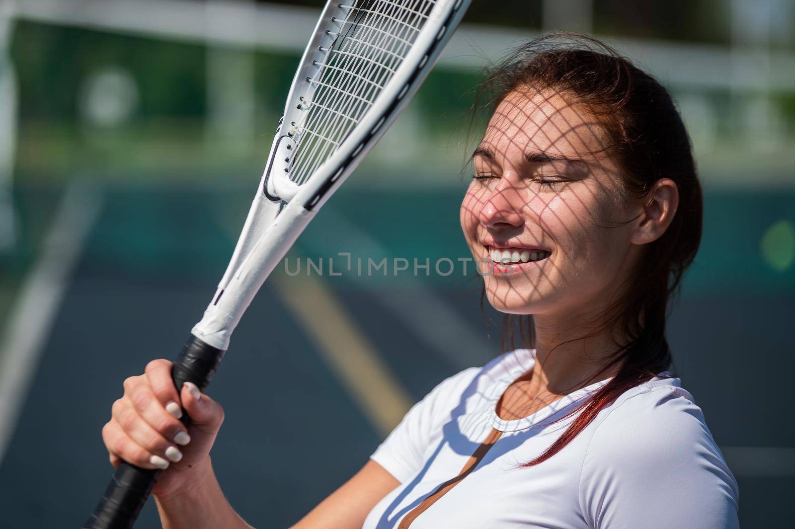 Beautiful smiling woman with a shadow from a tennis racket on her face on a sunny day by mrwed54