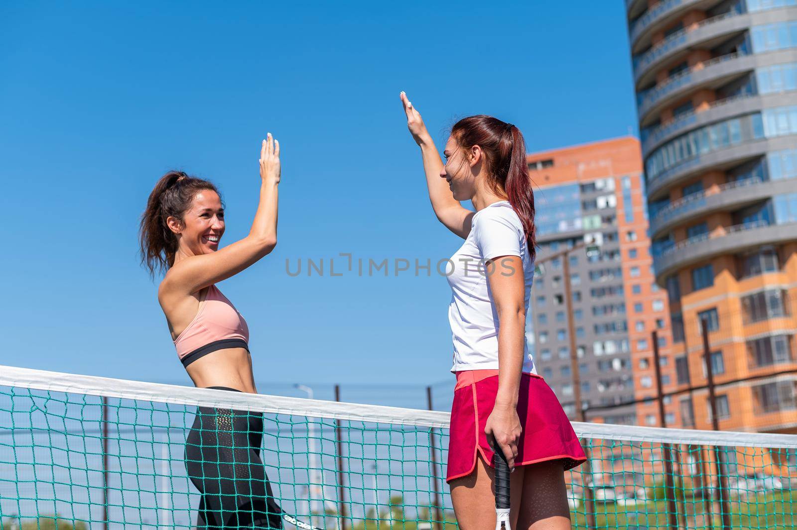 Two Caucasian women in sportswear greeting before a tennis match on an outdoor court. Players give a high five before the game