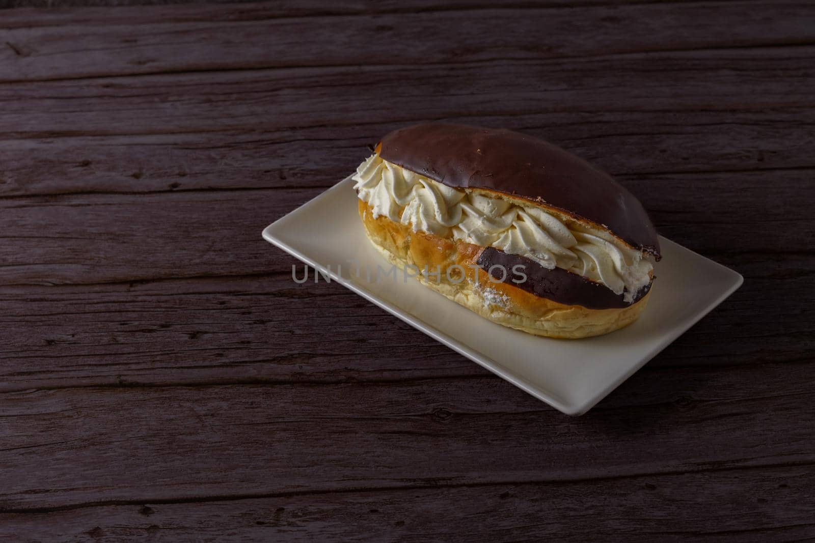 chocolate-covered cream-filled bun on a white plate on a wooden table