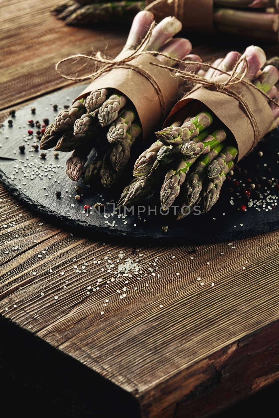 Bunches of an edible, delicious stems of asparagus on a stone slate, wooden table. Fresh, green vegetables with seasonings, top view. Healthy eating. Fall harvest, agricultural farming concept.