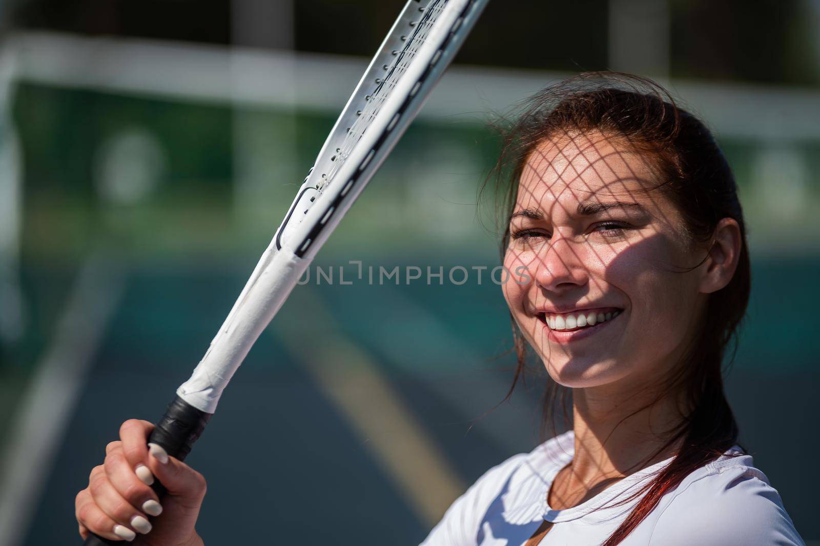 Beautiful smiling woman with a shadow from a tennis racket on her face on a sunny day.