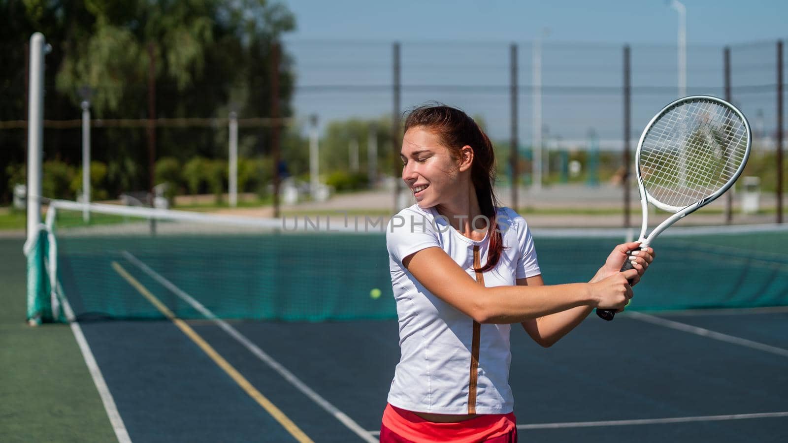 Young caucasian woman playing tennis on an outdoor court on a hot summer day