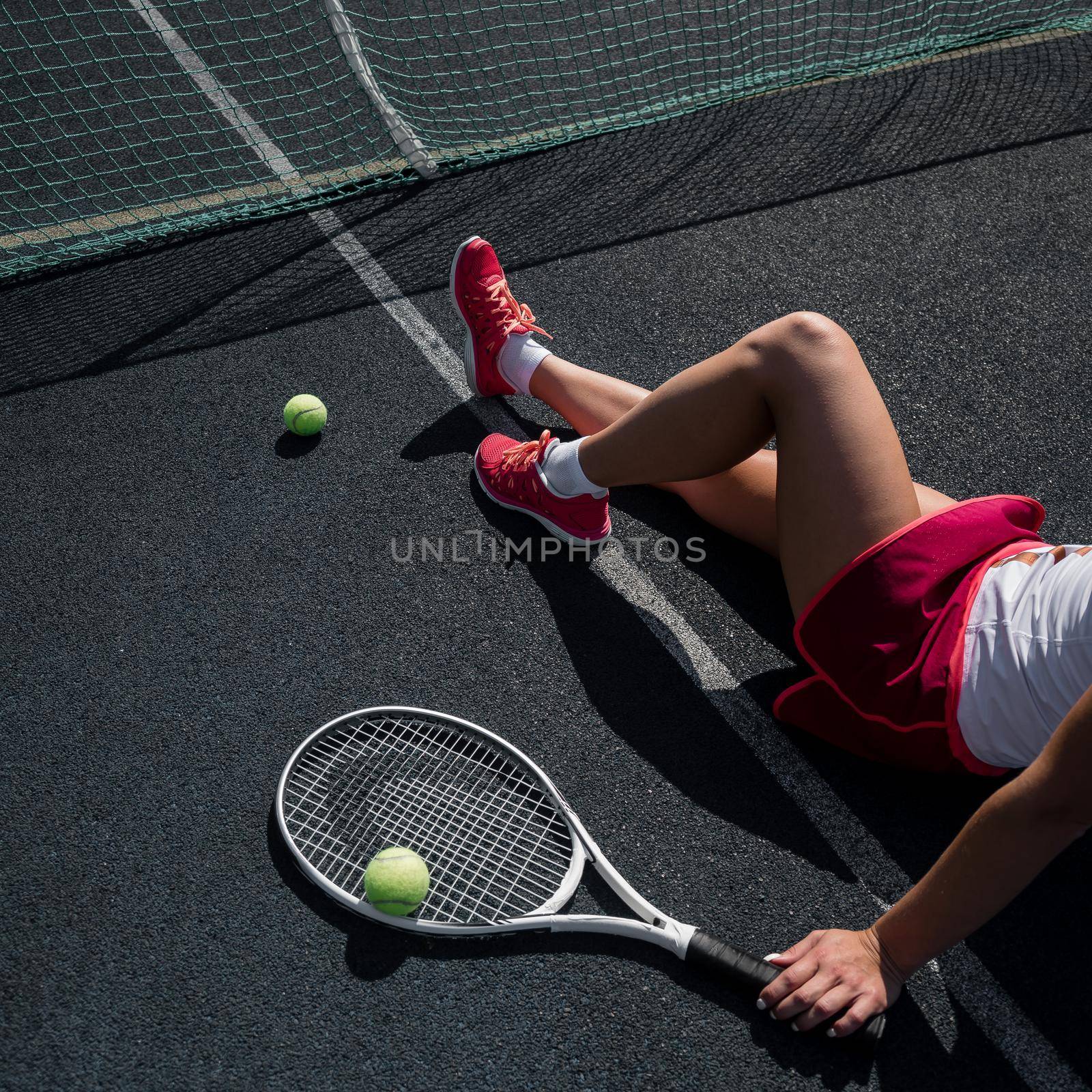 A faceless girl in a sports skirt sits on a tennis court and holds a rocket. Top view of female legs