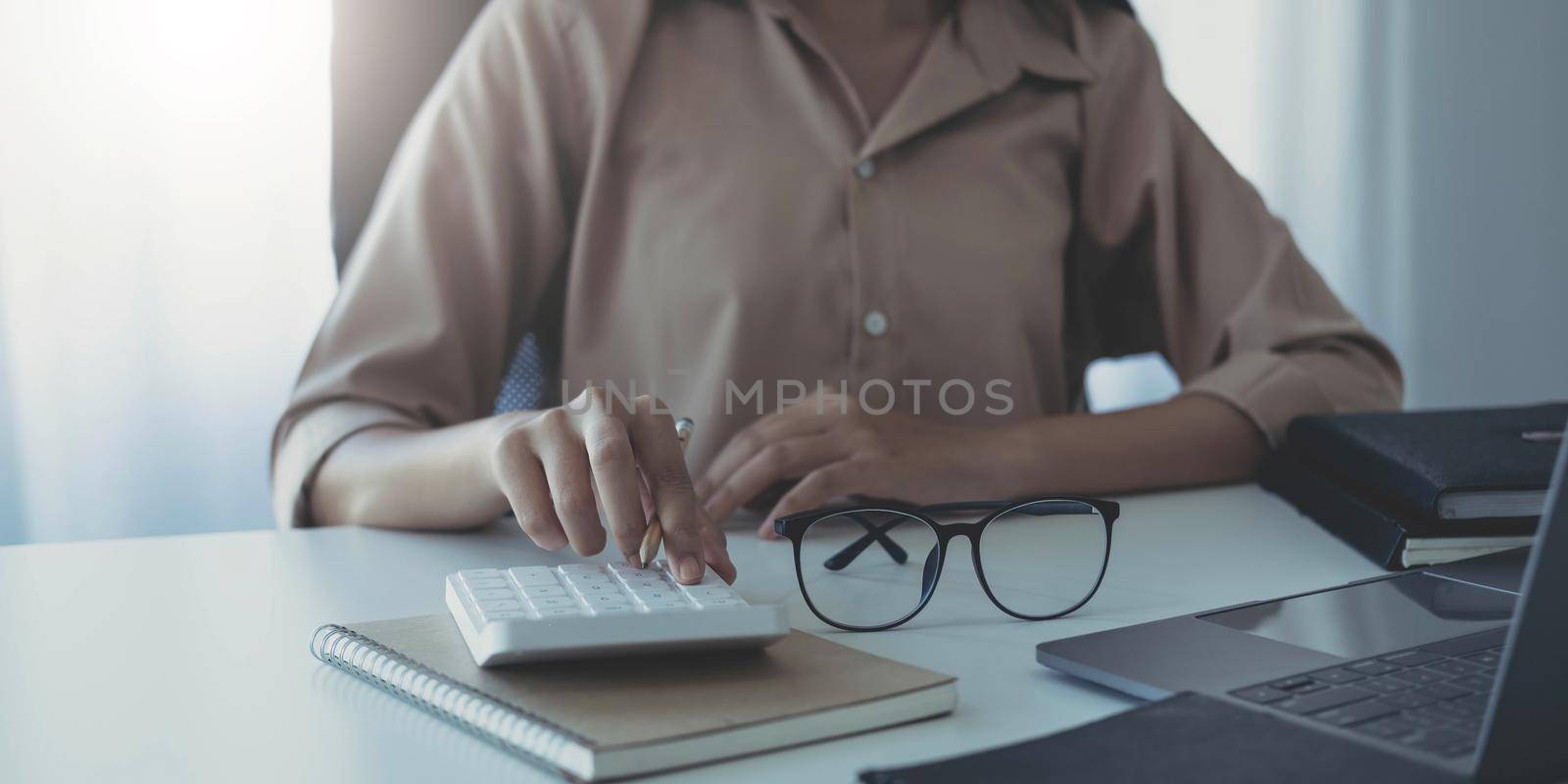 Business woman using calculator for do math finance on wooden desk in office and business working background, tax, accounting, statistics and analytic research concept by wichayada