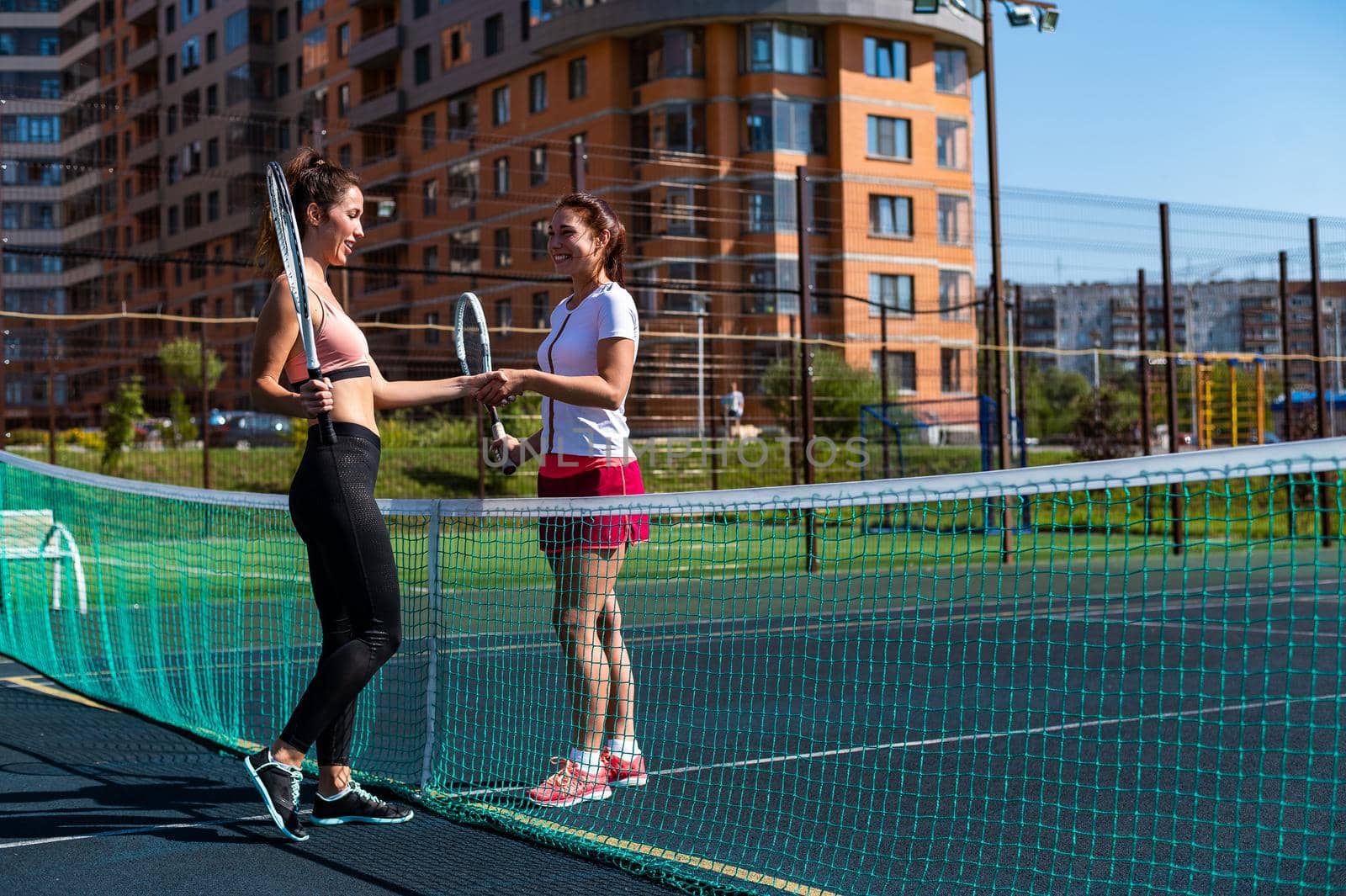 Two beautiful caucasian women in sportswear shake hands before a tennis match on an outdoor court