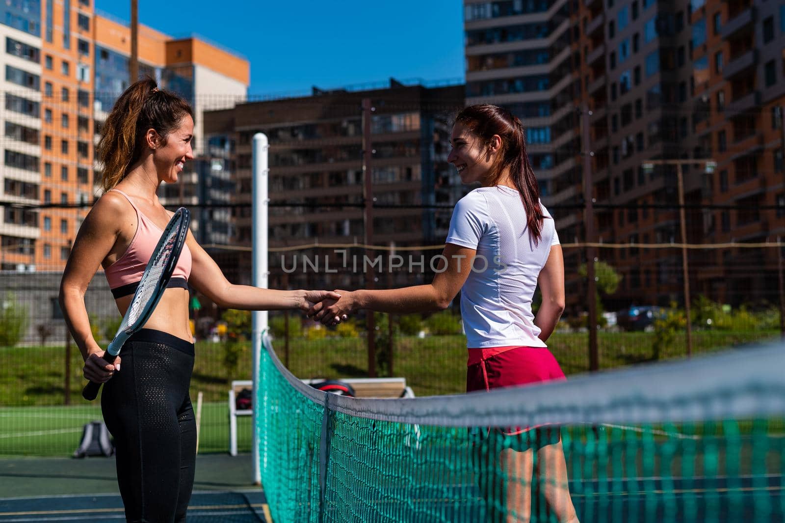 Two Caucasian women in sportswear shake hands after a tennis match on outdoor court. by mrwed54