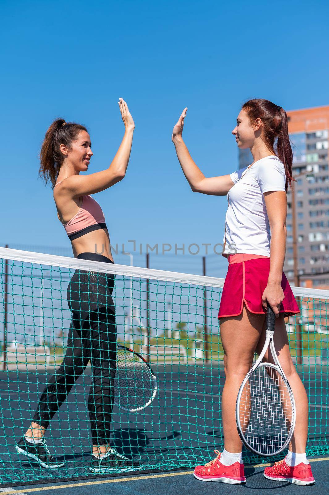 Two Caucasian women in sportswear greeting before a tennis match on an outdoor court. Players give a high five before the game
