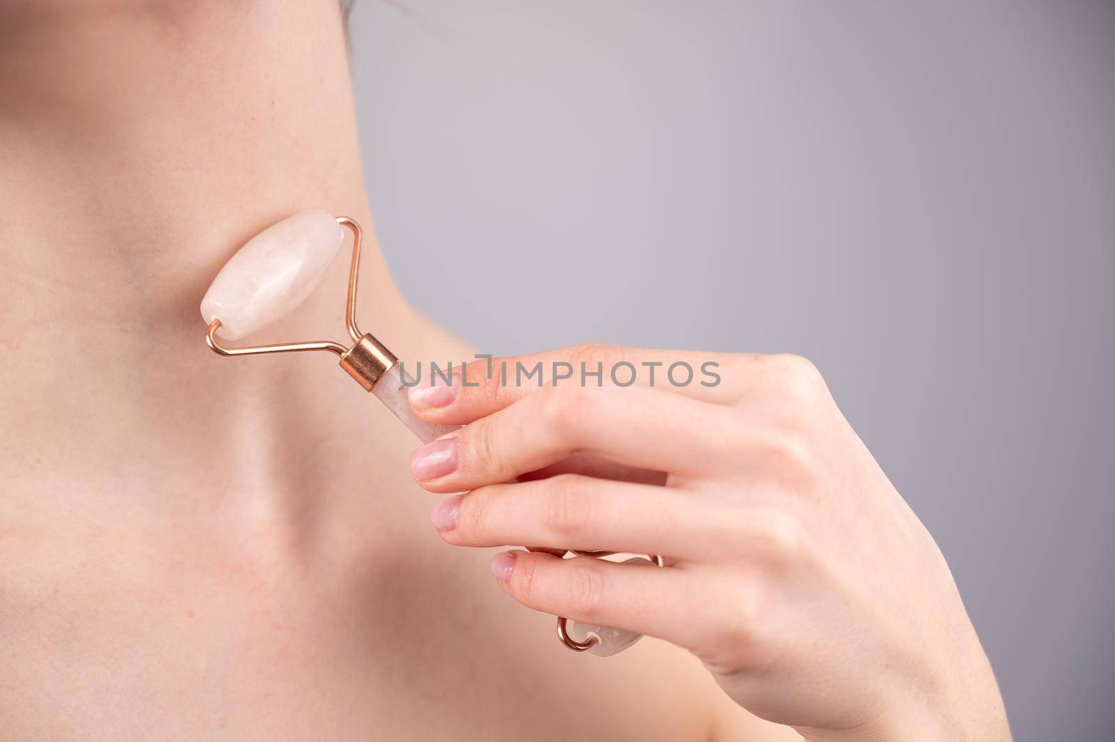 Close-up portrait of a woman using a quartz roller massager for an alternative fight against wrinkles on her neck. Smoothing of the rings of venus