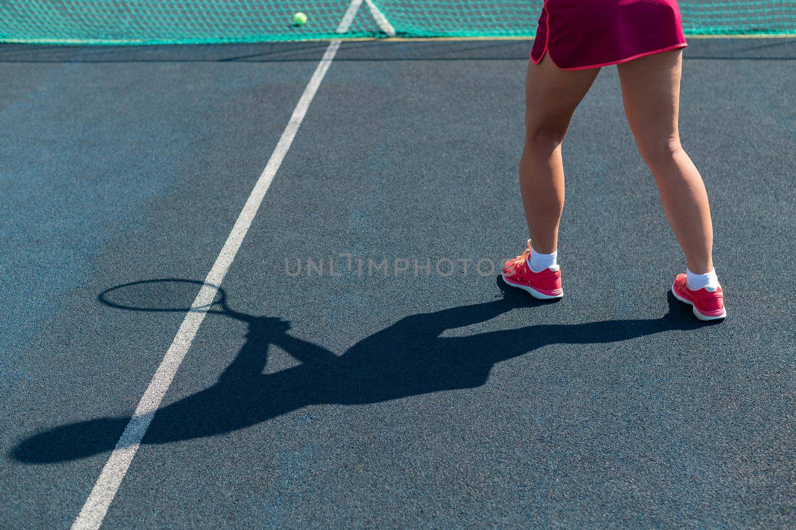 Shadow of woman tennis player. Close-up of female legs on an outdoor tennis court. by mrwed54