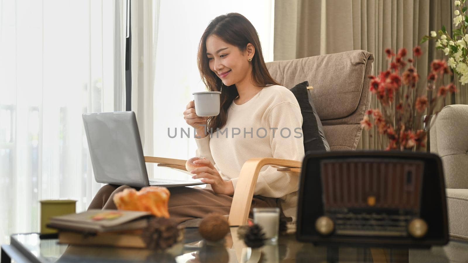 Happy young woman in warm woolen sweater drinking hot tea and using laptop in an autumn day by prathanchorruangsak