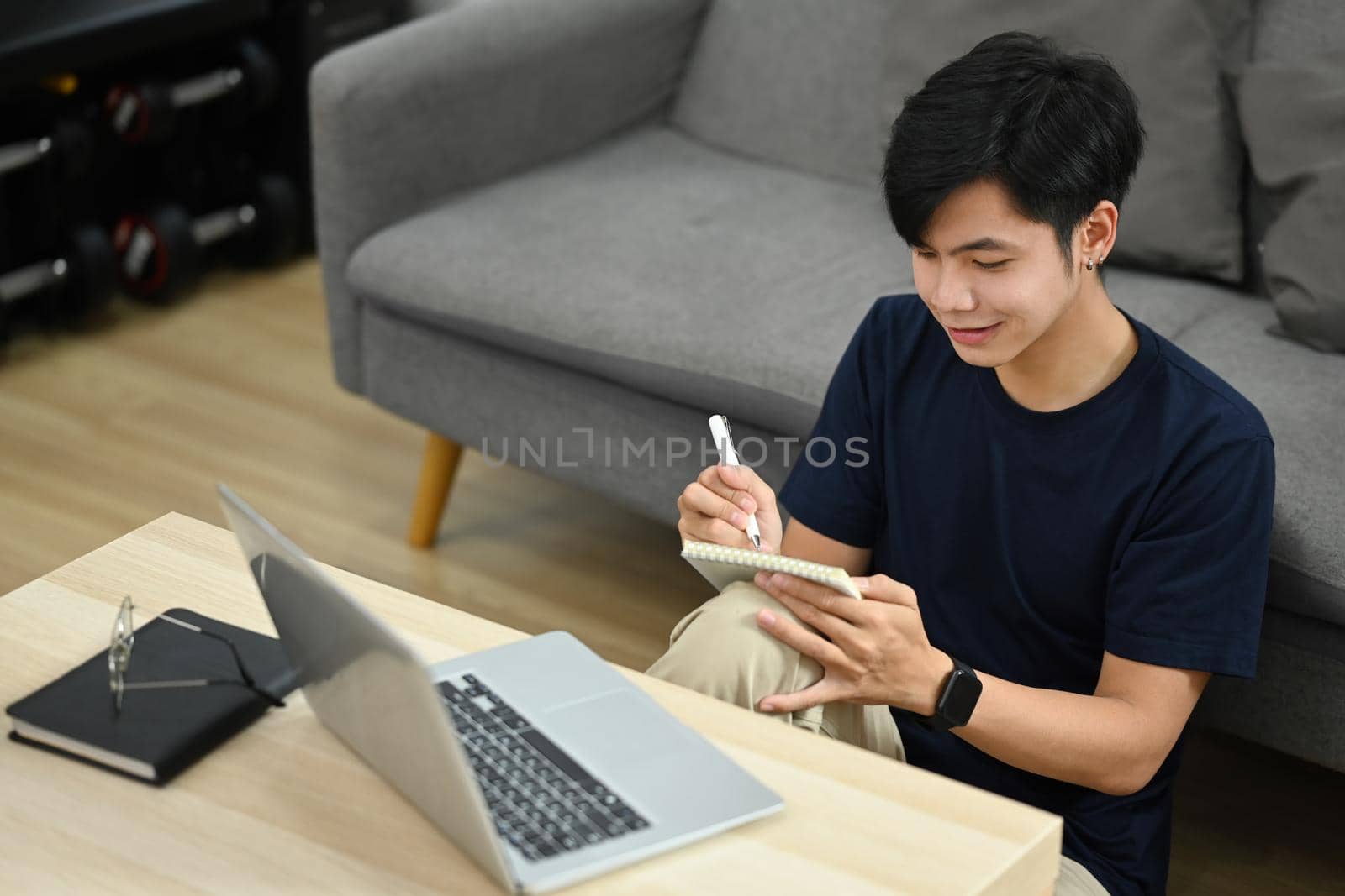 Asian male working, checking email in morning or searching information on laptop in bright living room.