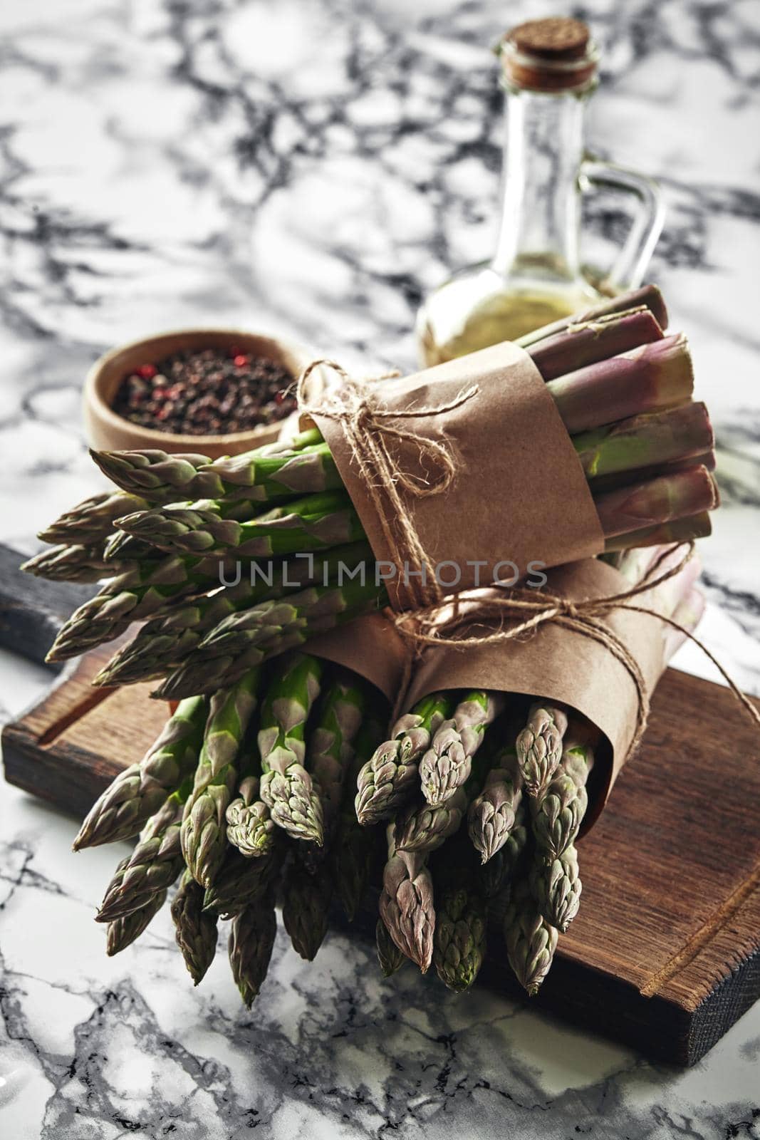 Bunch of an edible, green stems of asparagus on a wooden board, marble background. Fresh vegetables with olive oil and seasonings, top view. Healthy eating. Spring harvest, agricultural farming concept.