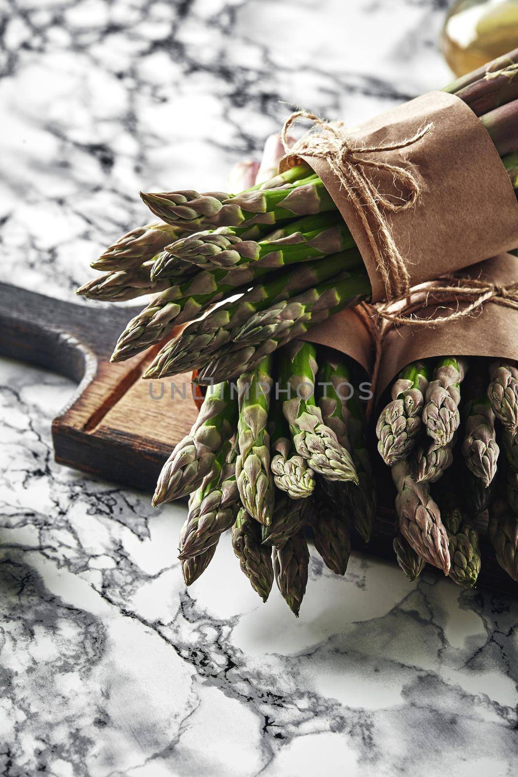 Bunch of an edible, ripe spears of asparagus on a wooden board, marble background. Fresh, green vegetables, top view. Healthy eating. Spring harvest, agricultural farming concept.