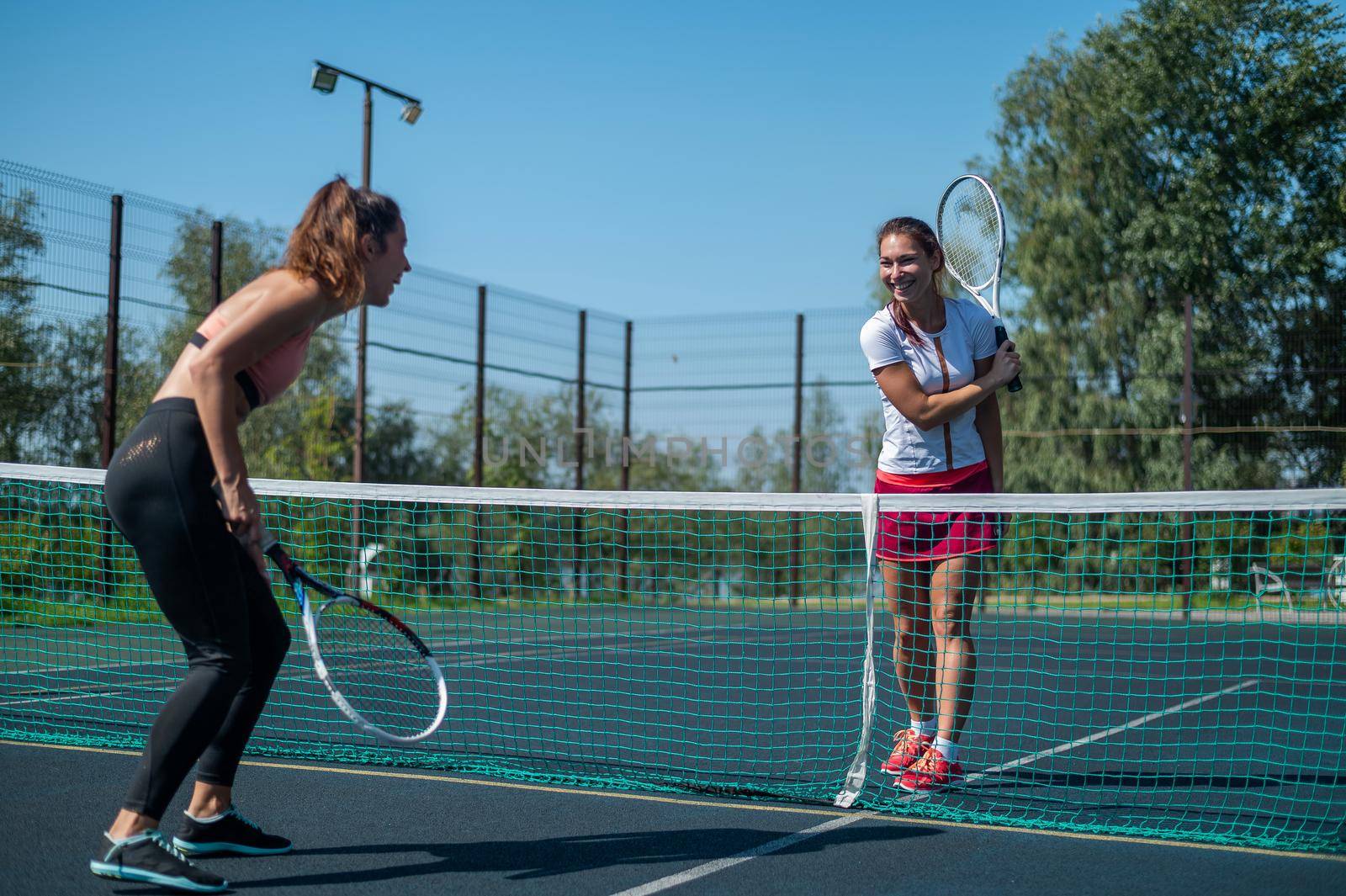 Two athletic young women play tennis on an outdoor court on a hot summer day
