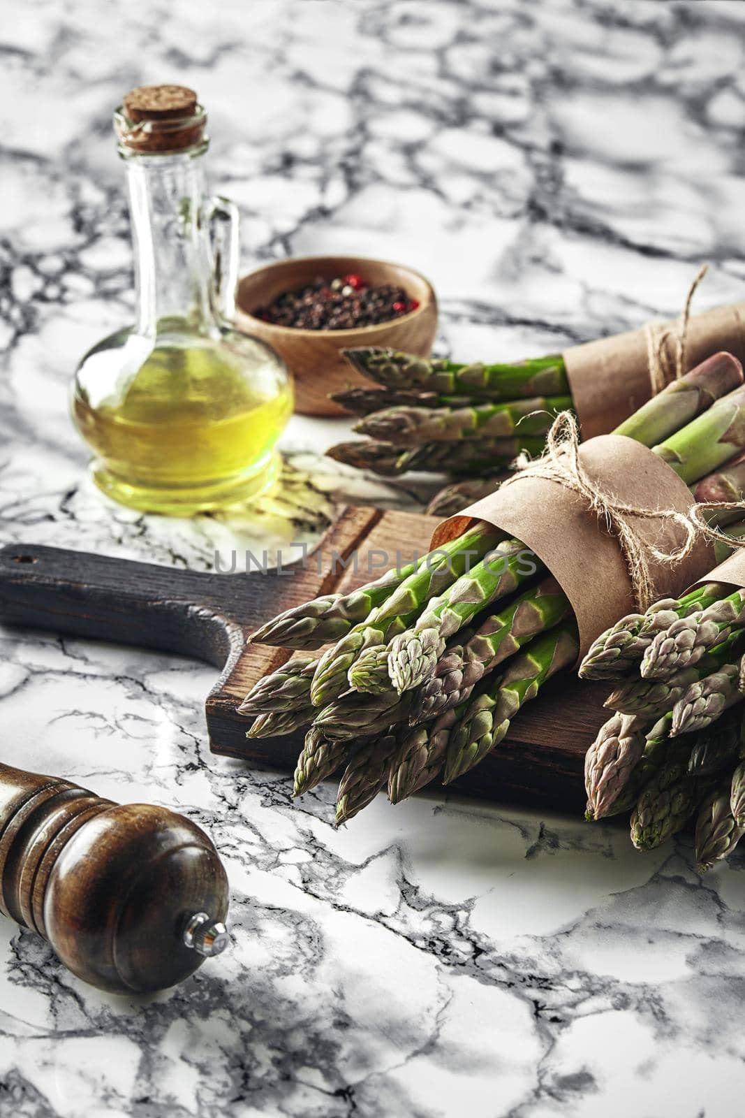 Bunch of an edible, raw sprouts of asparagus on a wooden board, marble background. Fresh, green vegetables with olive oil and seasonings. Healthy eating. Spring harvest, agricultural farming concept.