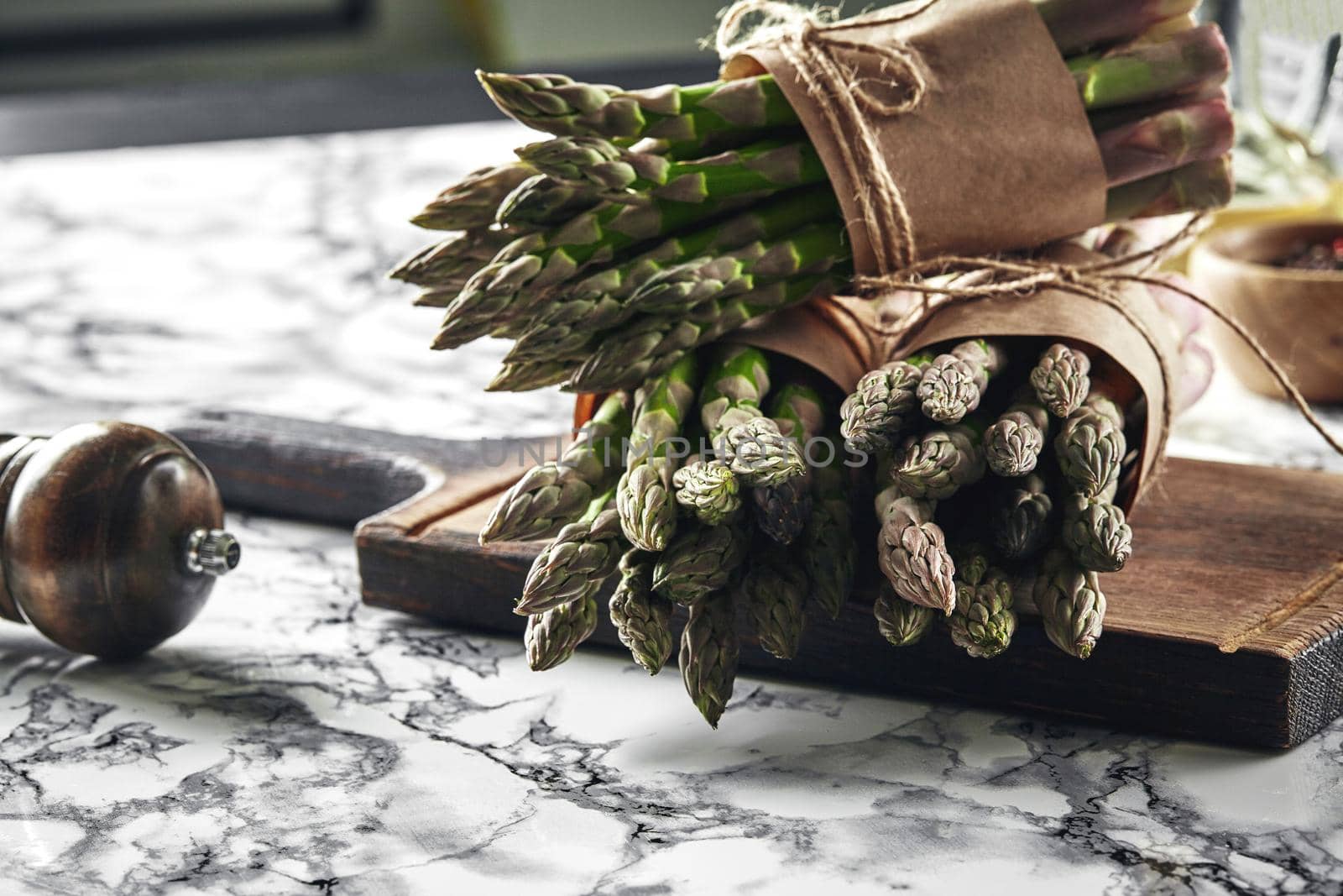 Bunch of an edible, ripe sprouts of asparagus on a wooden board, marble background. Fresh, green vegetables. Healthy food. Spring harvest, agricultural farming concept.