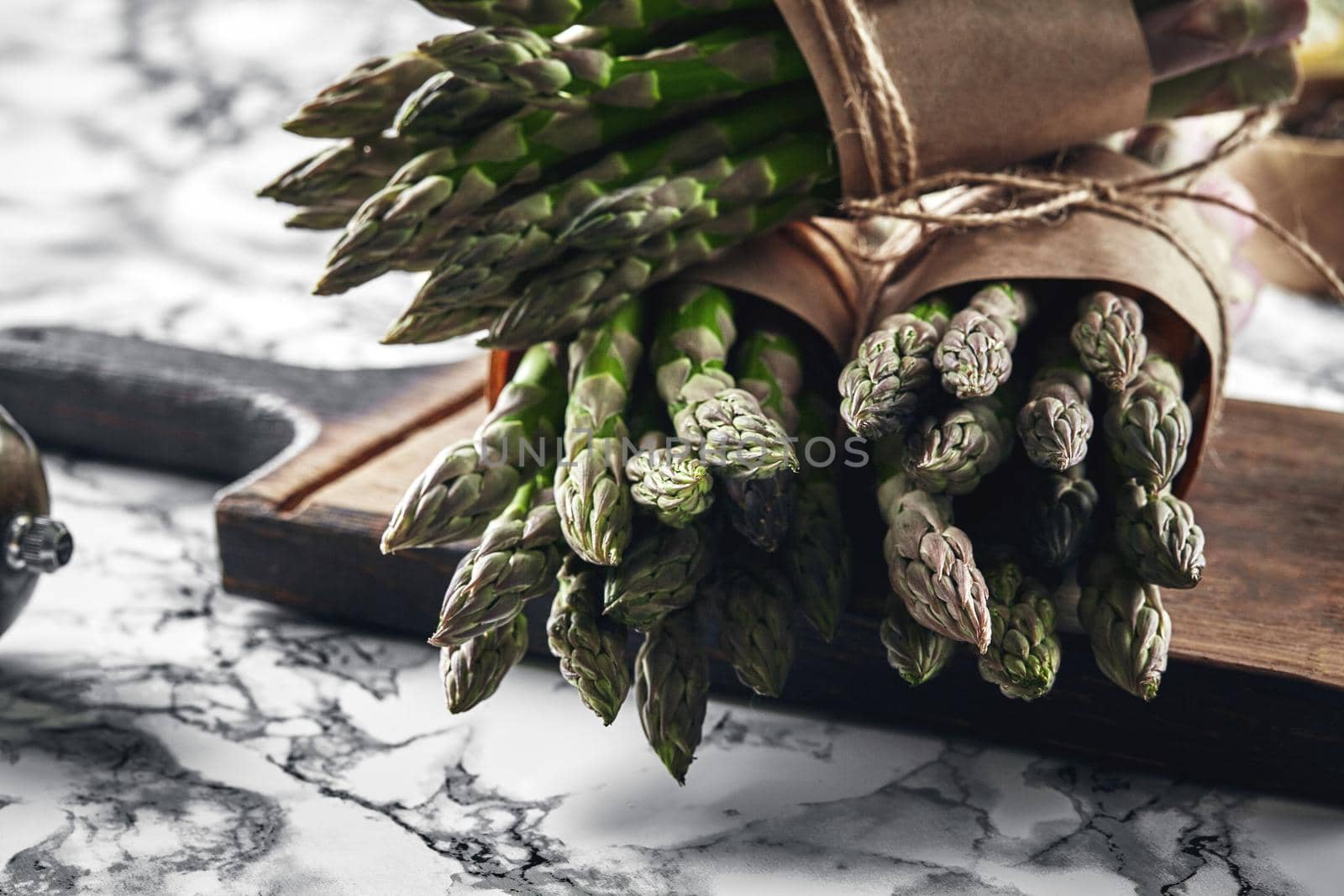 Bunch of an edible, ripe sprigs of asparagus on a wooden board, marble background. Fresh, green vegetables. Healthy eating. Spring harvest, agricultural farming concept.
