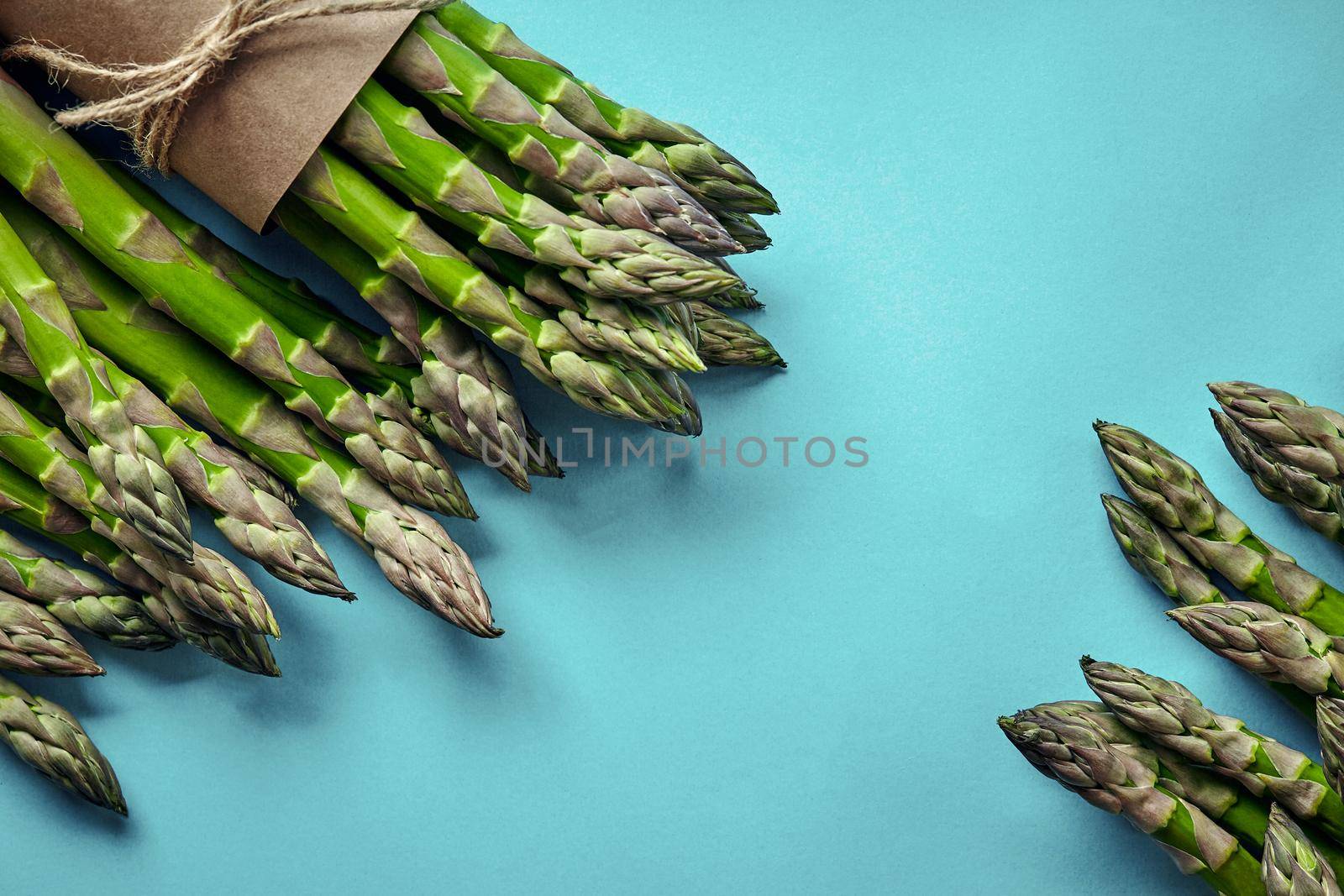 Bunch of an edible, green spears of asparagus isolated on blue background. Fresh vegetables, top view. Healthy eating. Spring harvest, agricultural farming concept.