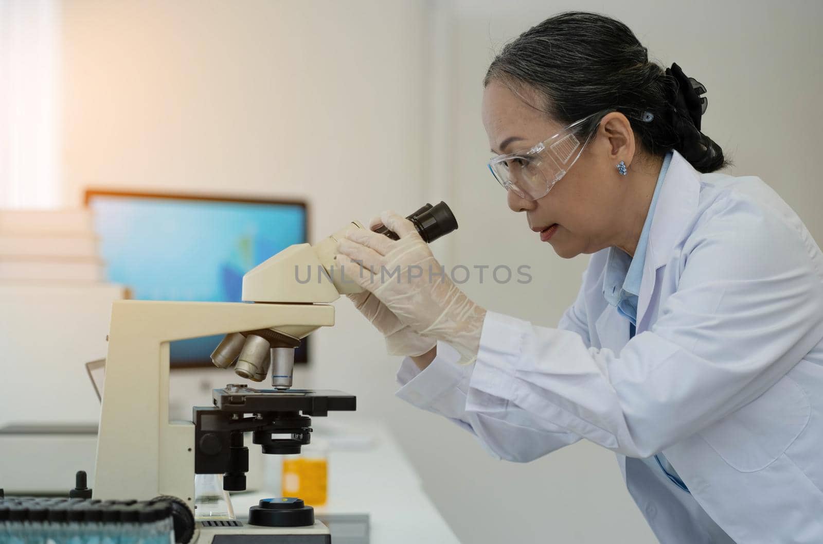 Medical Development Laboratory: Female Scientist Looking Under Microscope, Analyzes Petri Dish Sample. In Background Big Pharmaceutical Lab with Specialists Conducting Medicine, Biotechnology Research.