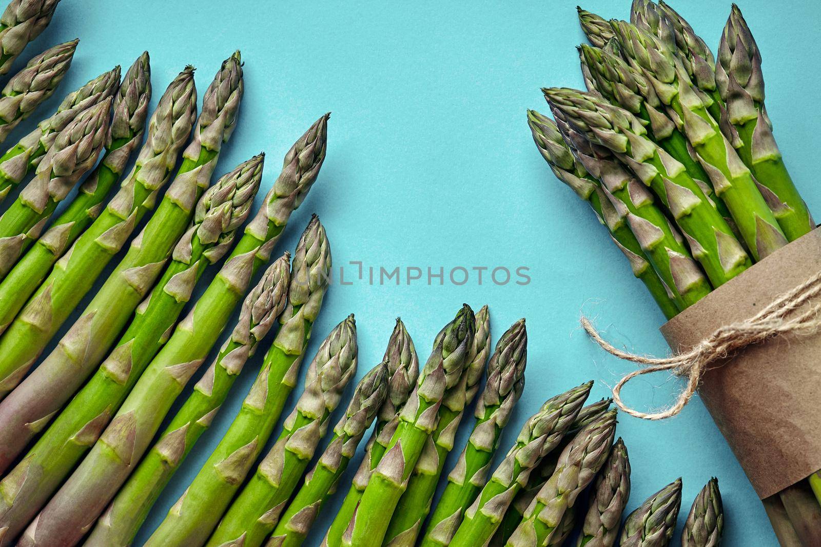 Bunch of an edible, raw stems of asparagus on blue background. Fresh, green vegetables, top view. Healthy eating. Spring harvest, agricultural farming concept.