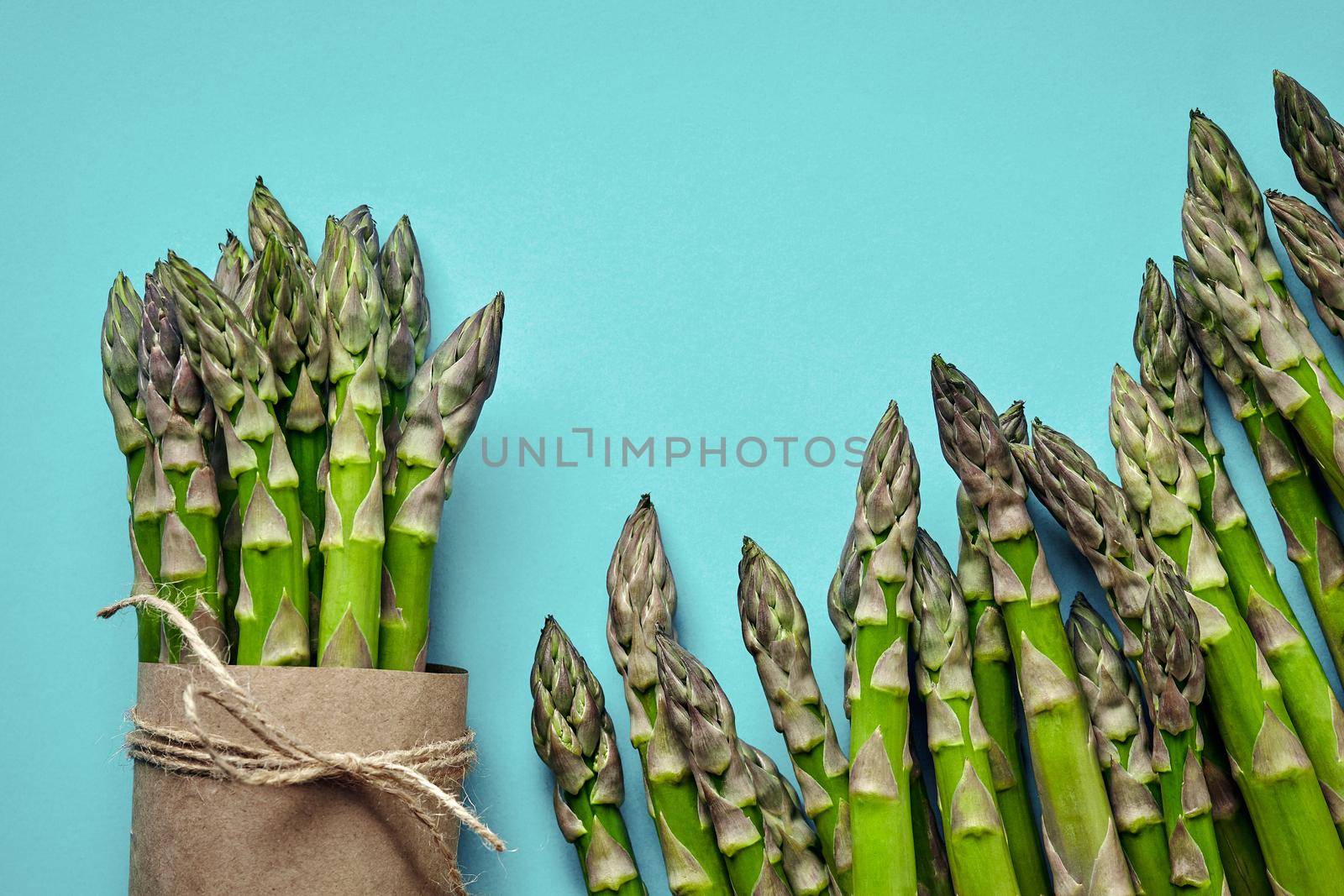 Bunch of an edible, fresh stalks of asparagus isolated on blue background. Green vegetables, top view. Healthy meal. Spring harvest, agricultural farming concept.