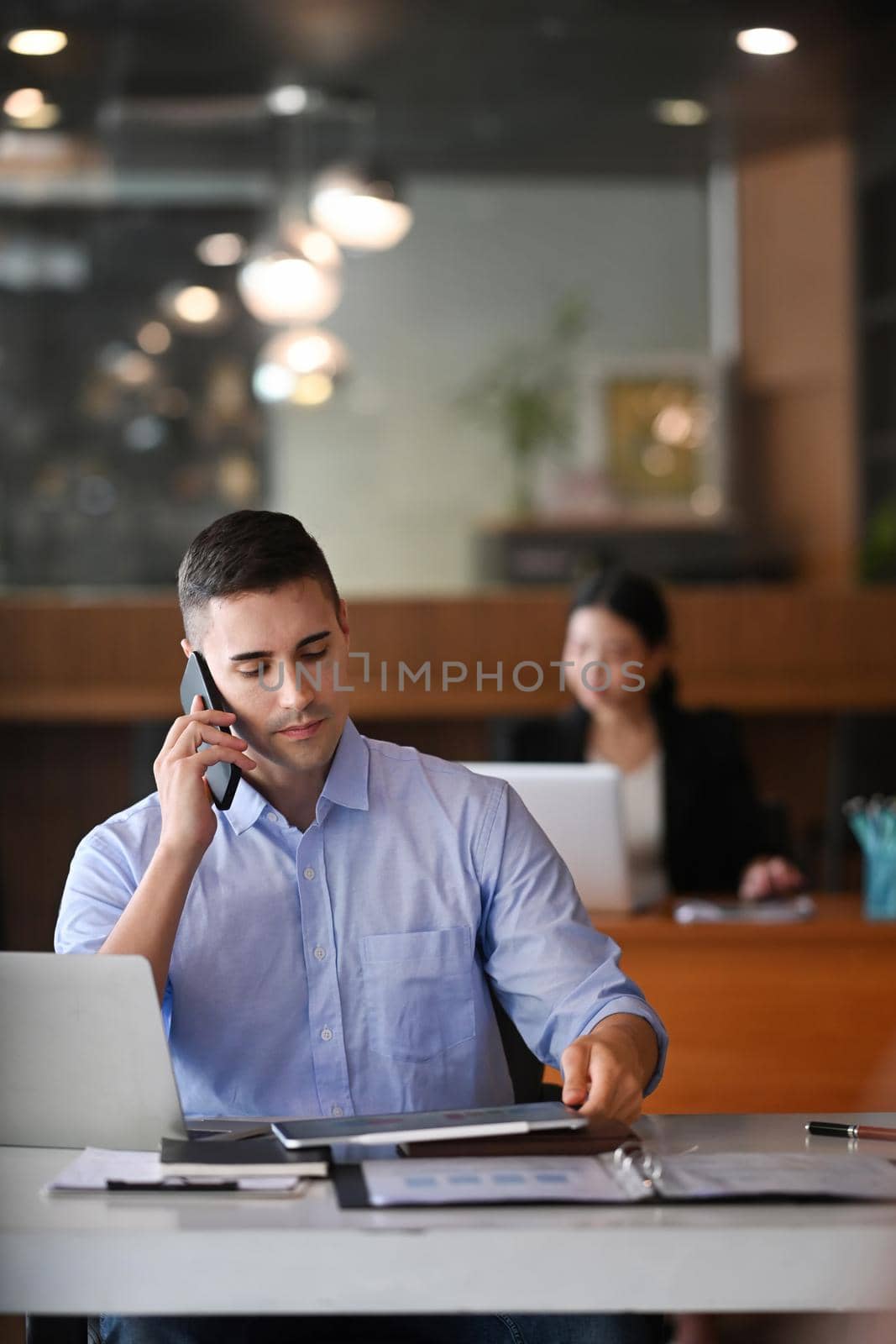 Businessman talking on mobile phone and reading reports in office. by prathanchorruangsak