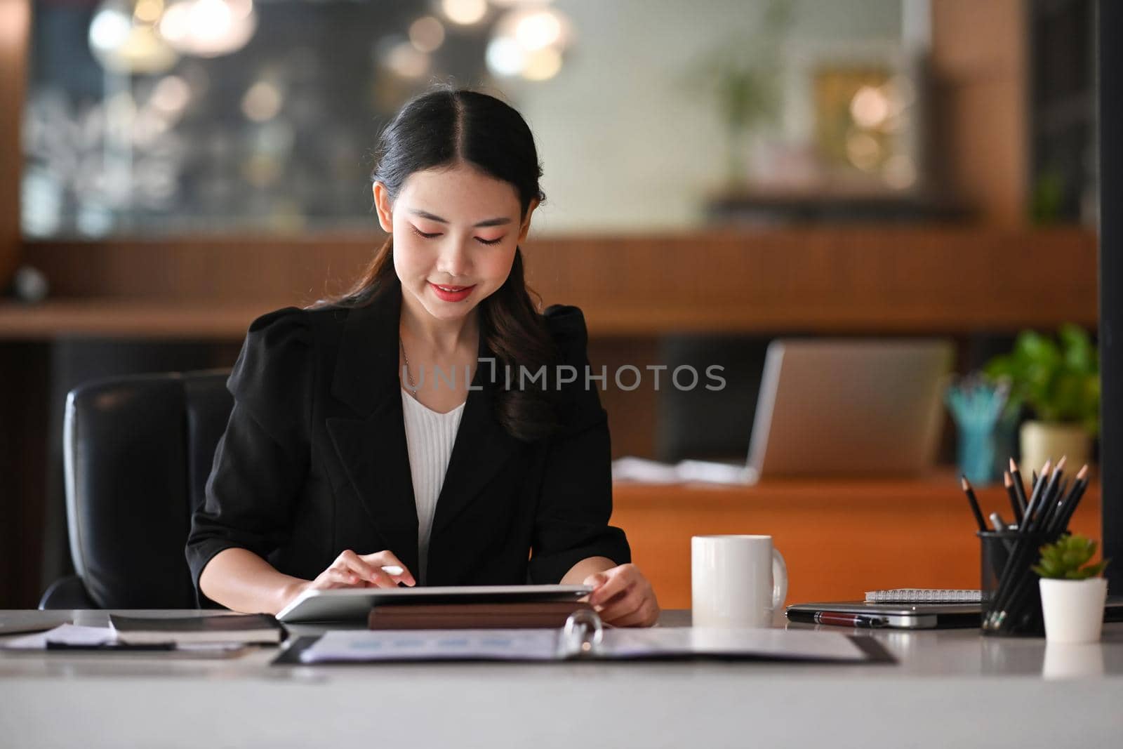 Young asian woman entrepreneur sitting in modern office and working with digital tablet. by prathanchorruangsak