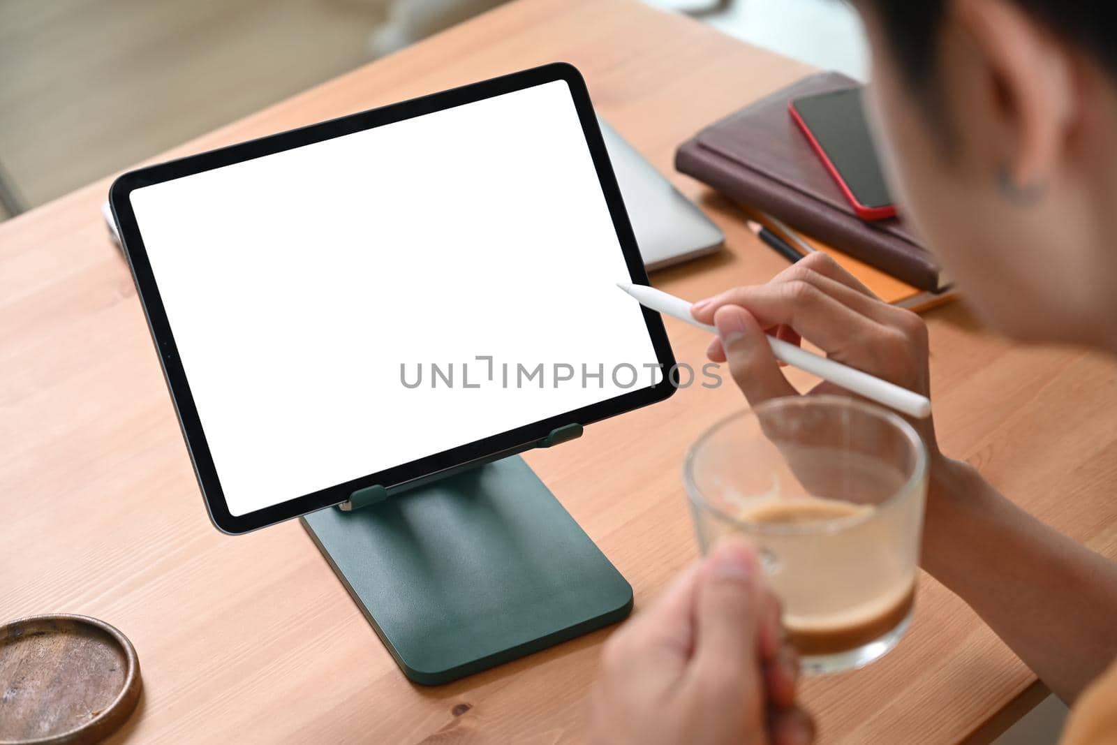 Cropped shot young man drinking coffee and using digital tablet on wooden table. by prathanchorruangsak