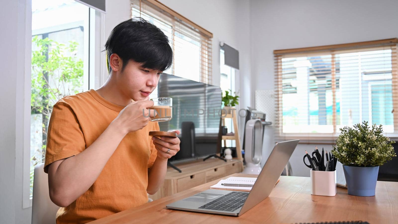 Casual man drinking coffee and using laptop computer at home. by prathanchorruangsak
