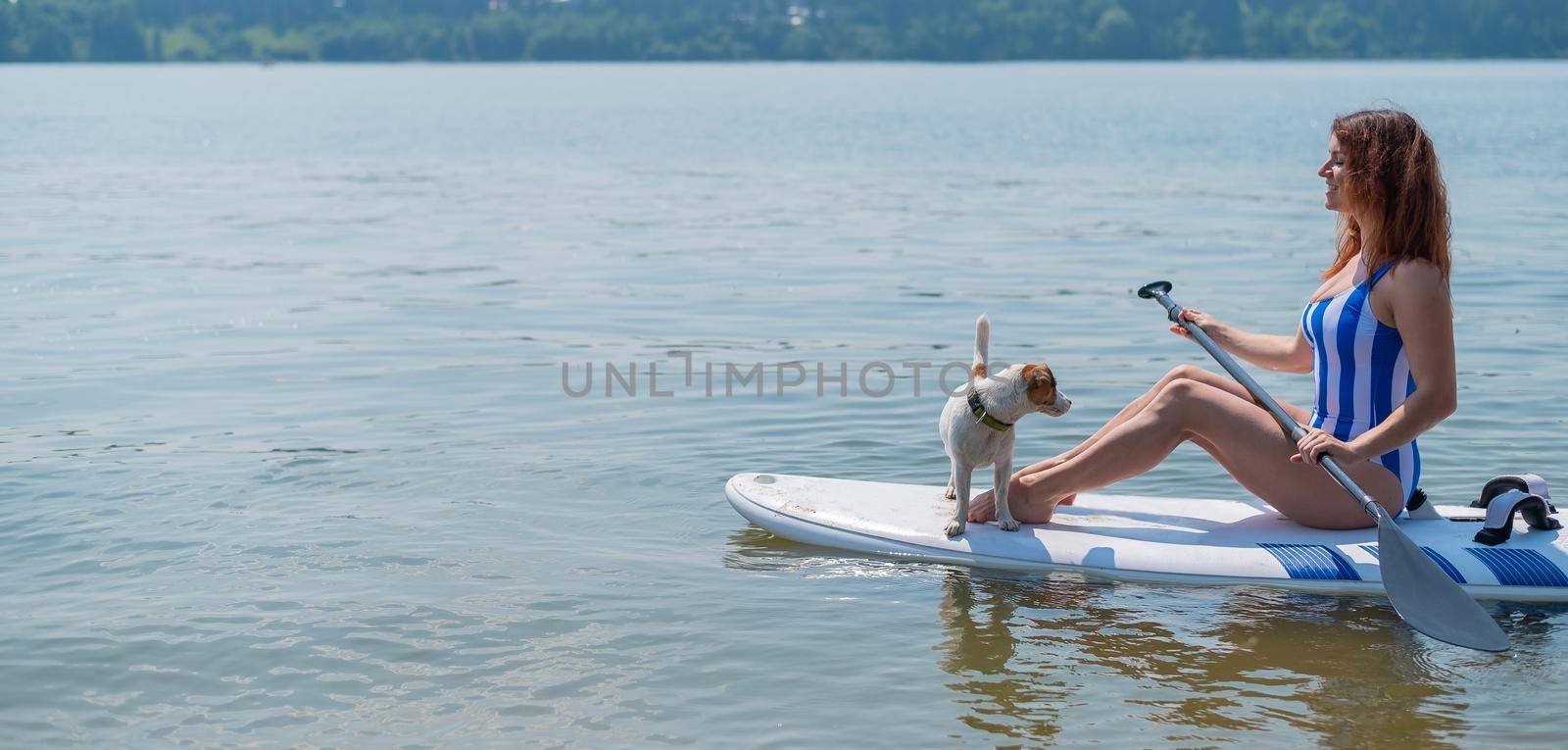 A woman is riding a sup surfboard with a dog on the lake by mrwed54