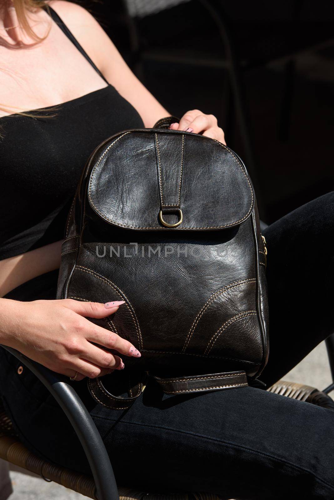 Woman with a brown leather backpack with antique and retro look. Outdoors photo. Black top and jeans