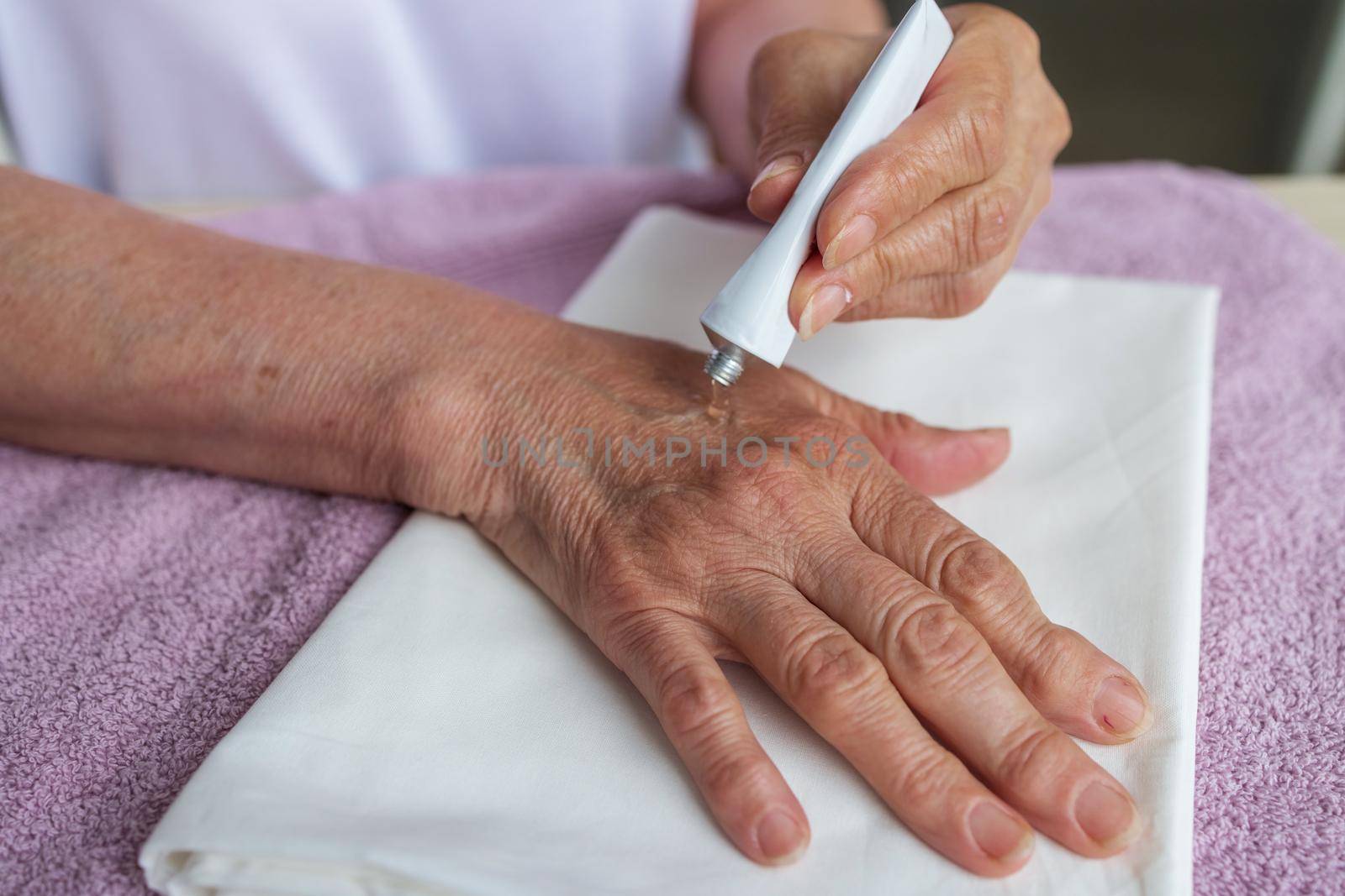 an elderly woman applies healing cream for arthritis on her old hands, medicine by Ramanouskaya