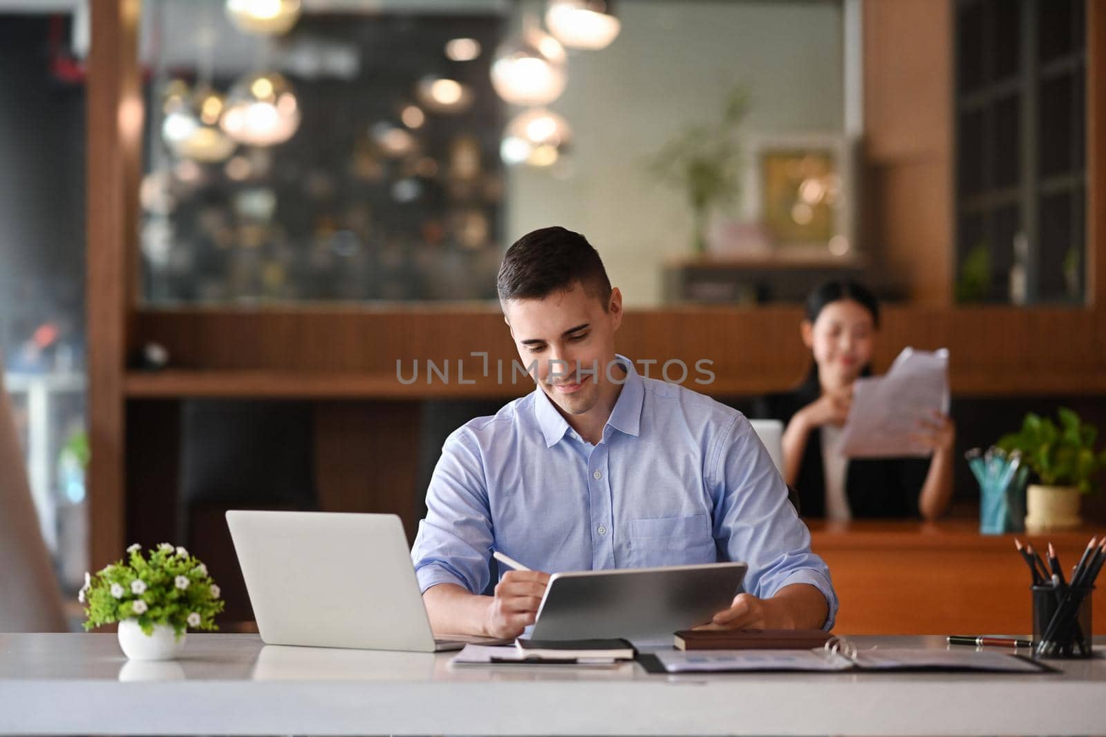 Smiling handsome businessman using digital tablet wile sitting in office.