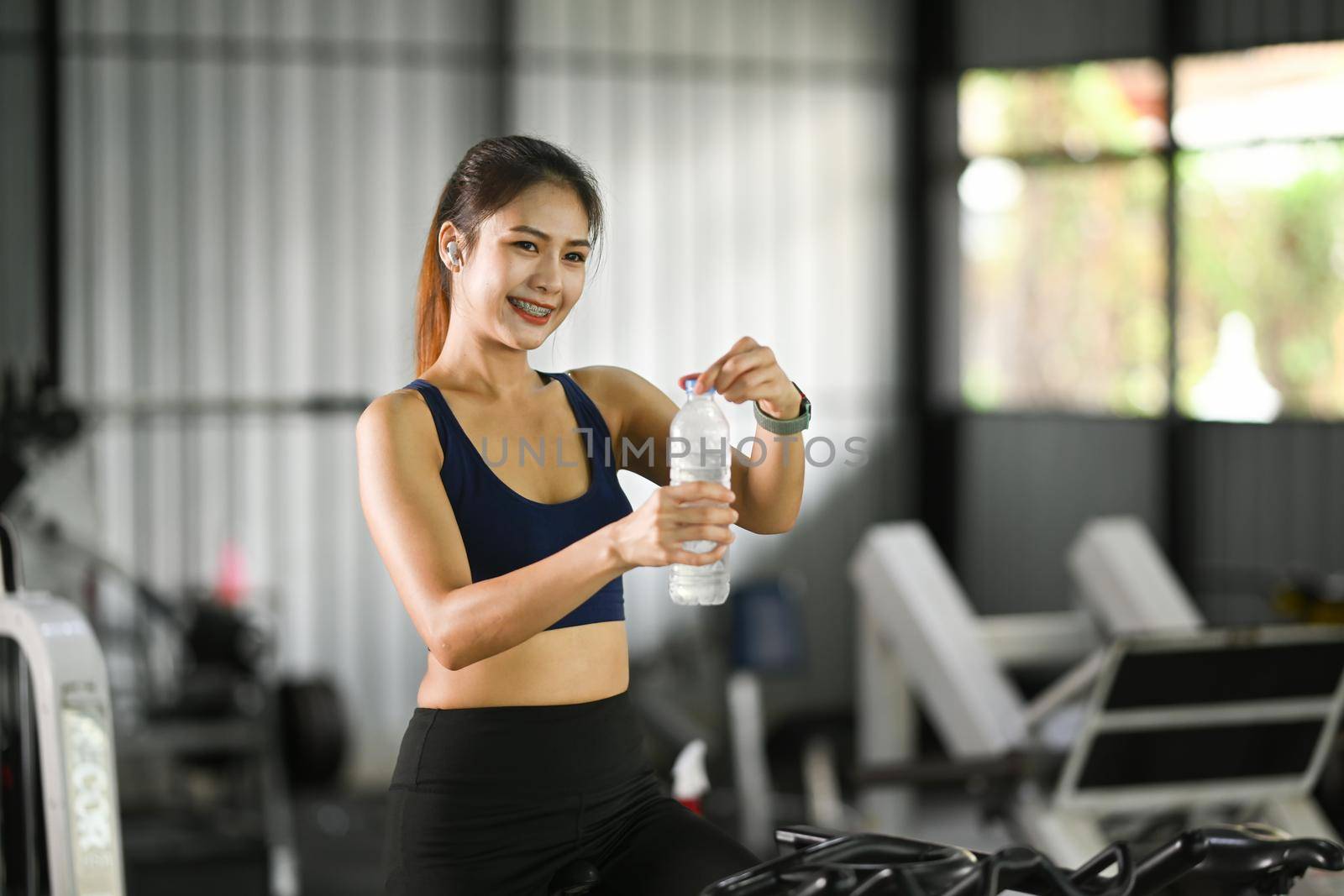 Smiling woman in sportswear drinking water and taking a break after workout.
