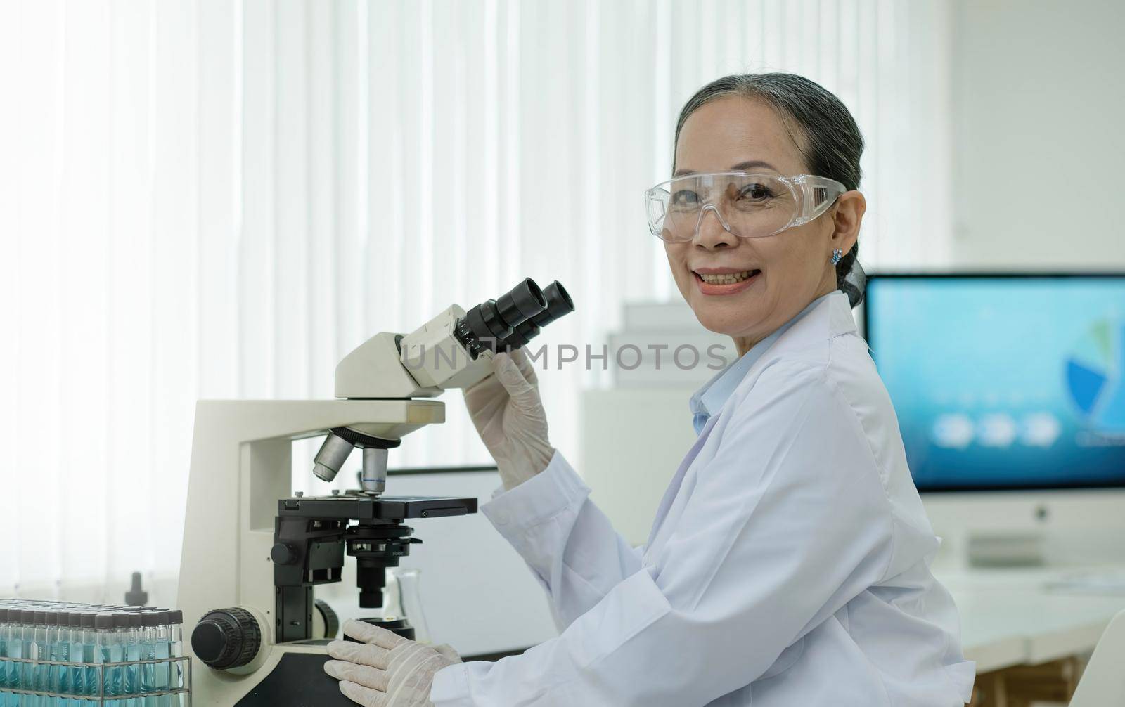 Modern Medical Research Laboratory: Portrait of a Professor female scientist using a microscope smiling charmingly on camera Advanced scientific laboratory for medicine biotechnology microbiological development by wichayada