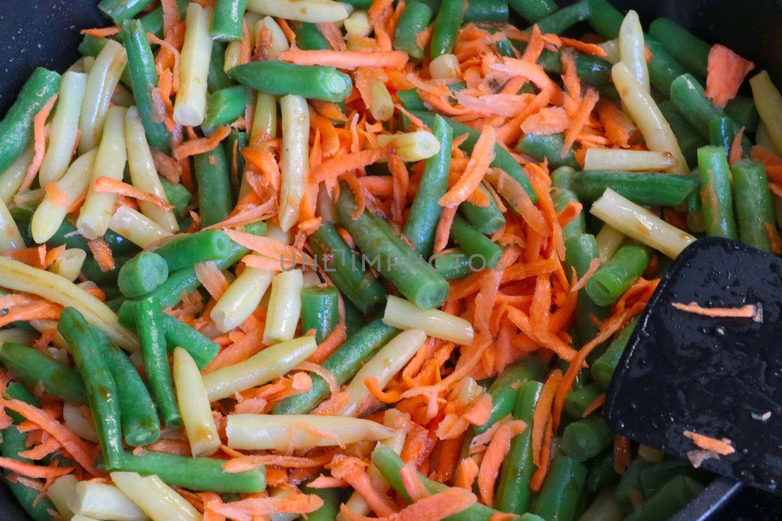 Asparagus beans with carrots are cooked in a pan