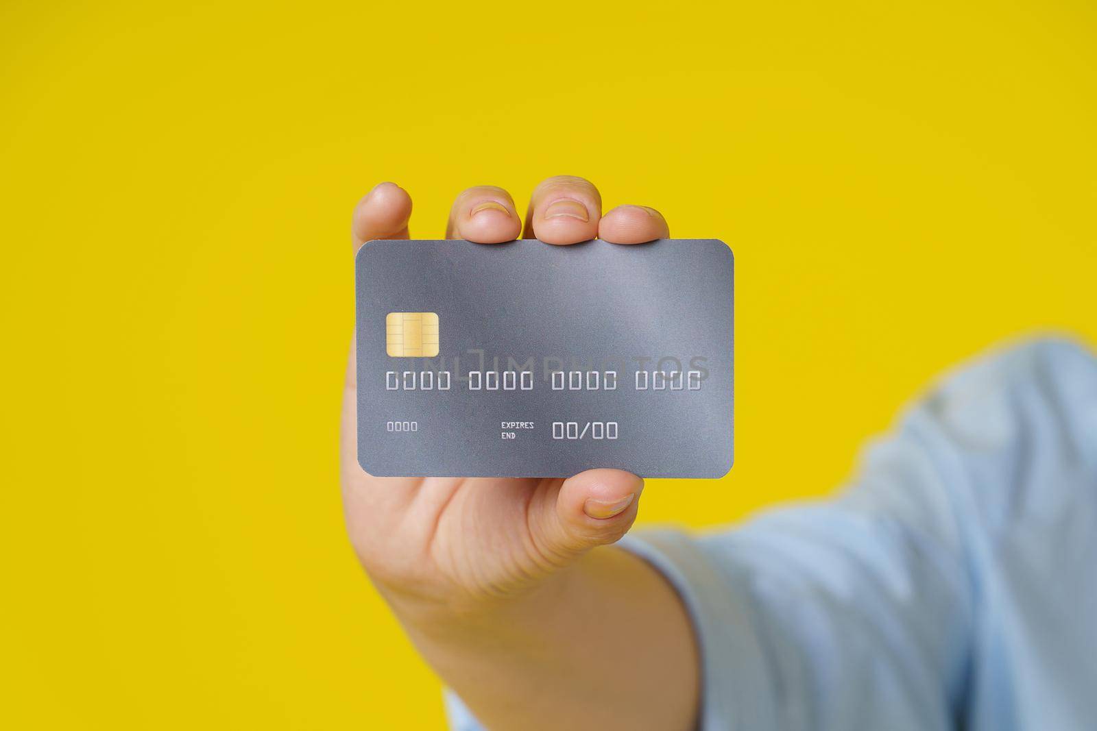Credit, debit cad close up in hand of mature woman showing it on camera, customer online payment or shopping online, isolated on yellow background. E-commerce, online banking concept.