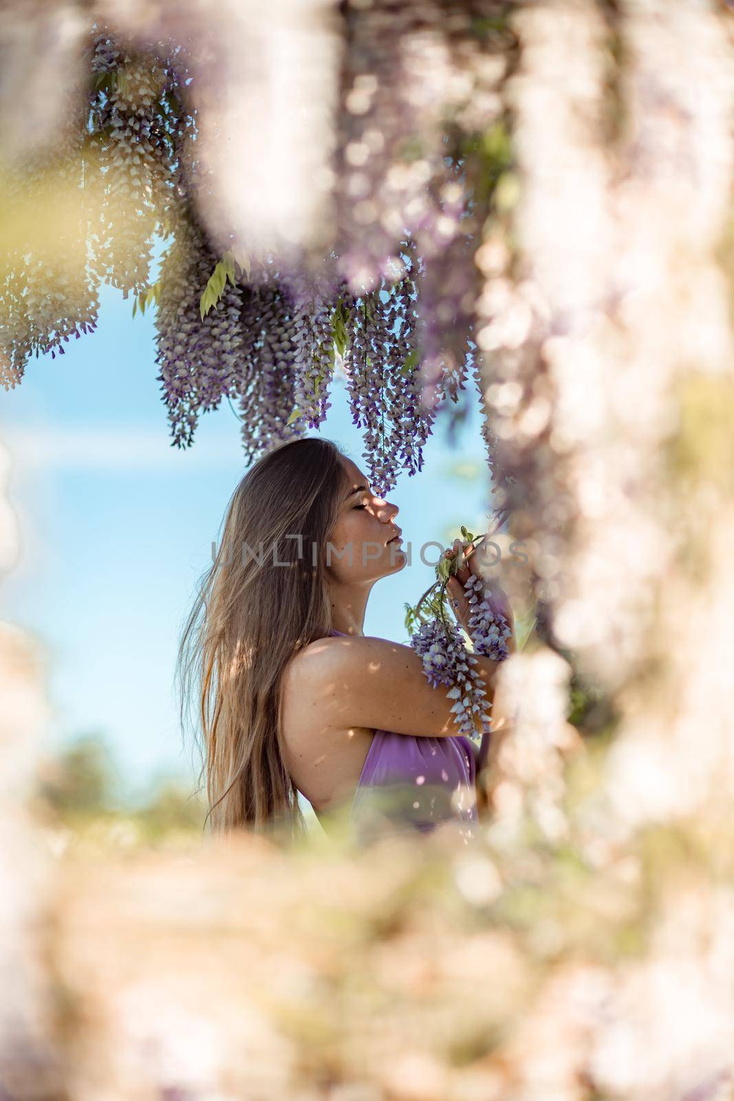 Thoughtful happy mature woman surrounded by chinese wisteria in purple dress by Matiunina