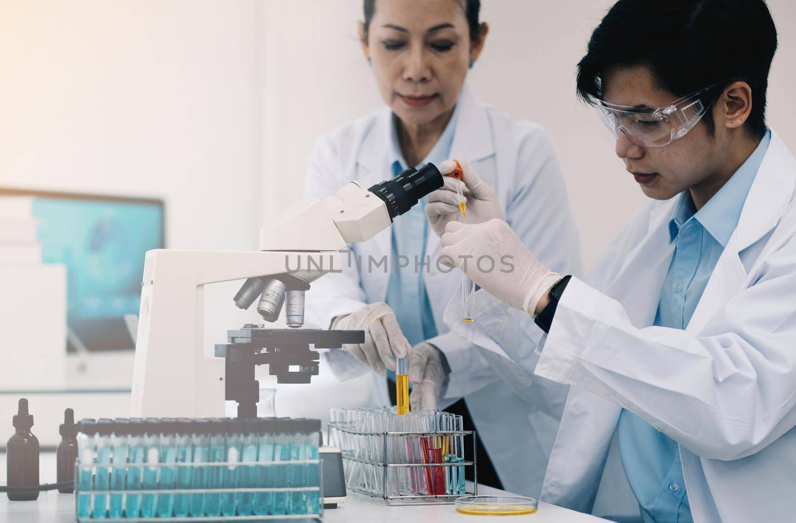 Health care researchers working in life science laboratory. Young female research scientist and senior male supervisor preparing and analyzing microscope slides in research lab. by wichayada