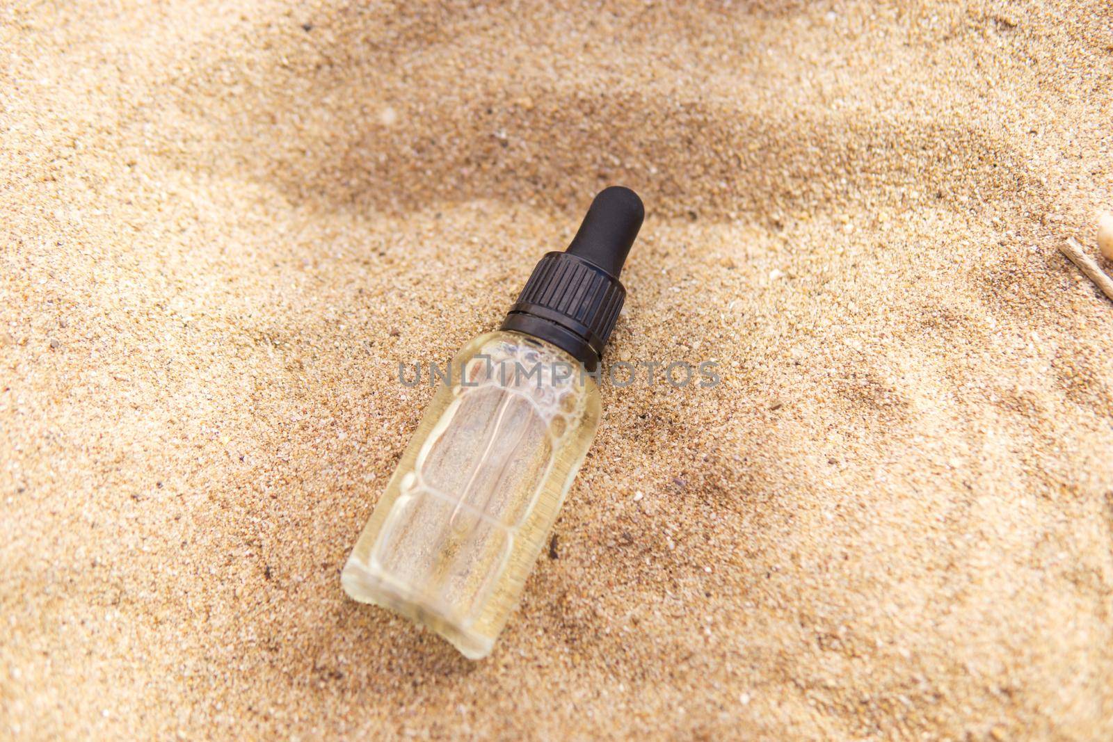 Cosmetic serum for the skin in a glass bottle. A bottle with a pipette on a sandy beach by the sea. Essences for skin care on a sandy background. The concept of natural cosmetics and SPA products.